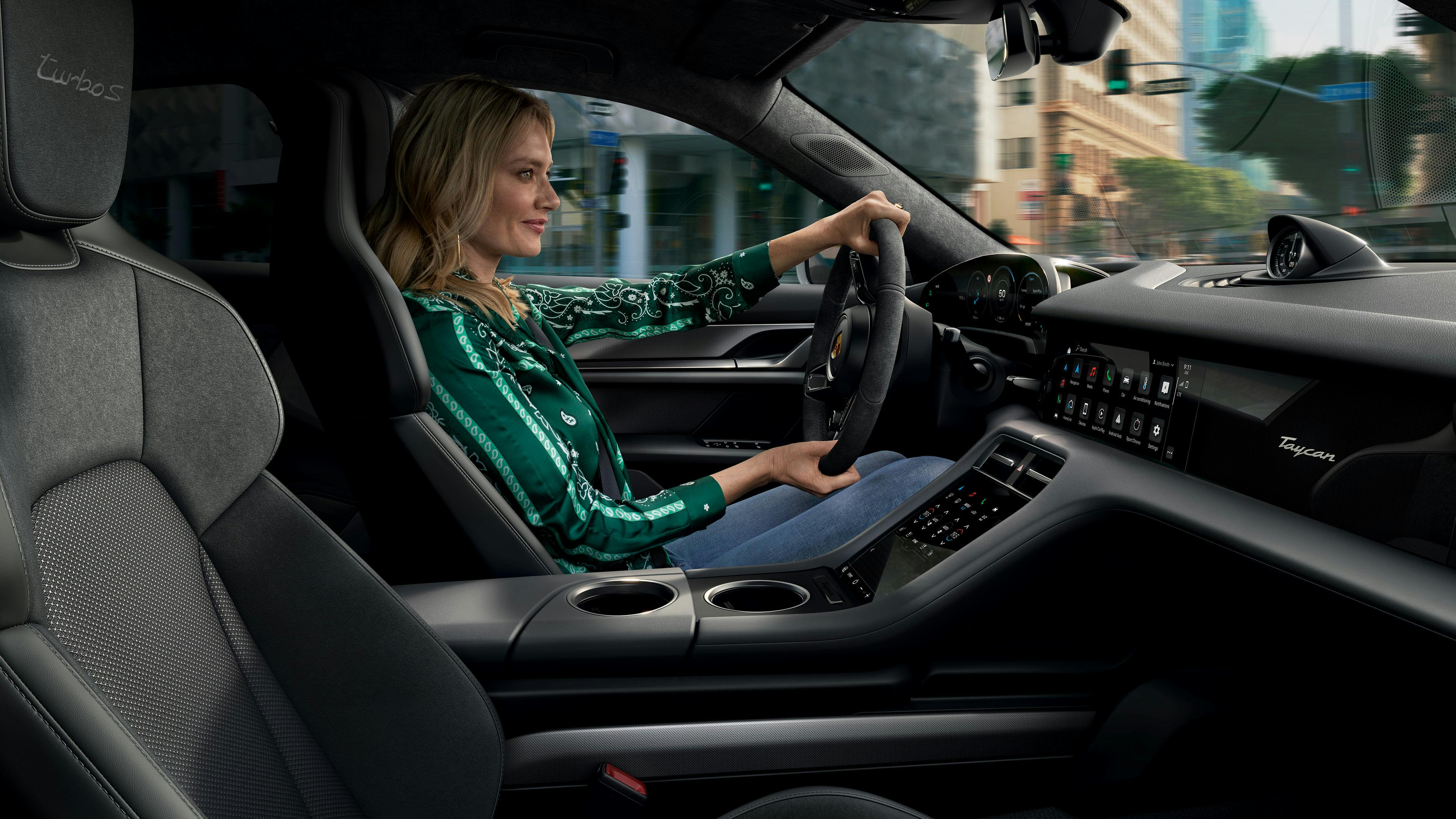 Blonde woman in green blouse driving Taycan in the city.