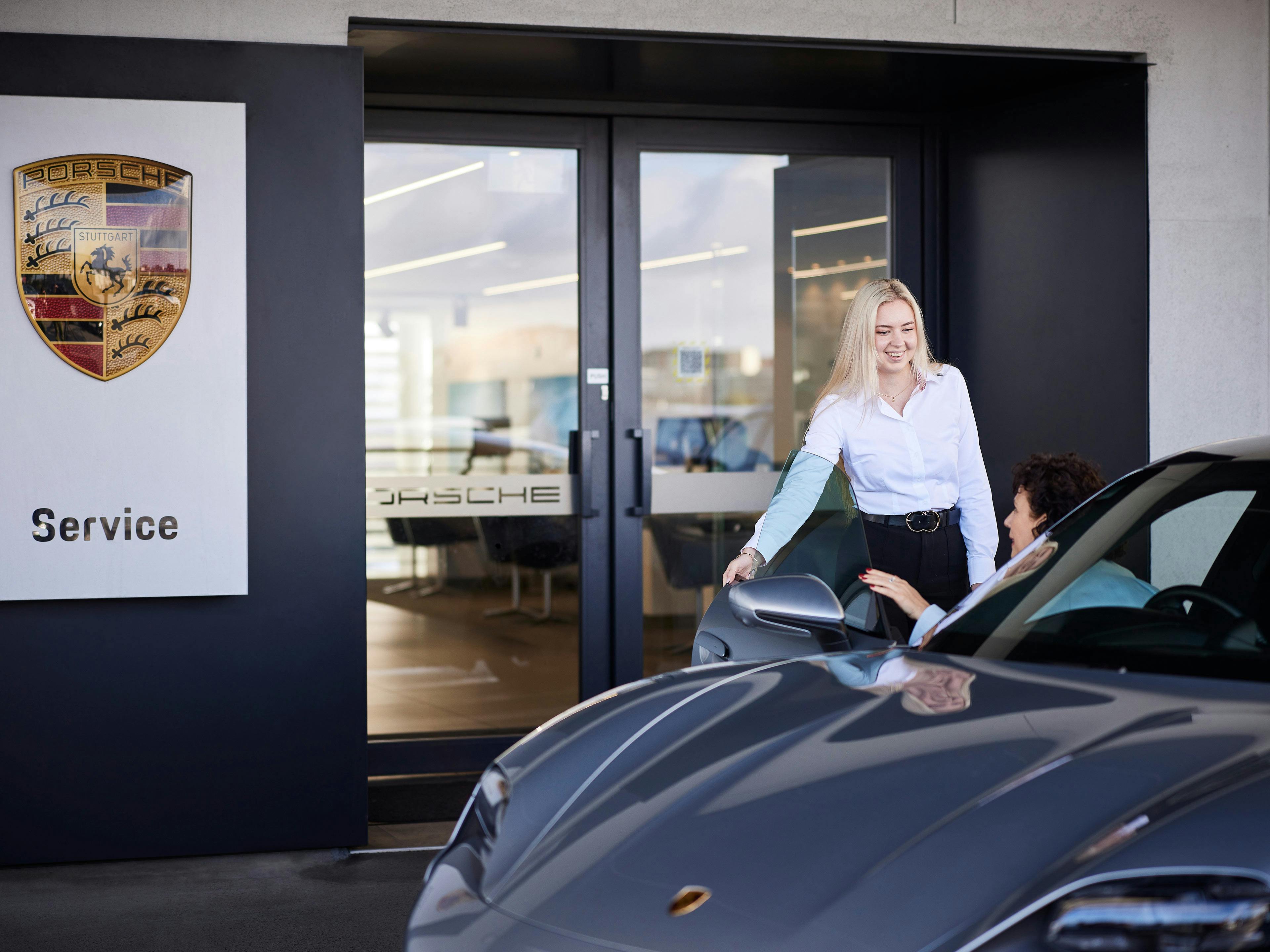Porsche service consultant greeting customer in car.