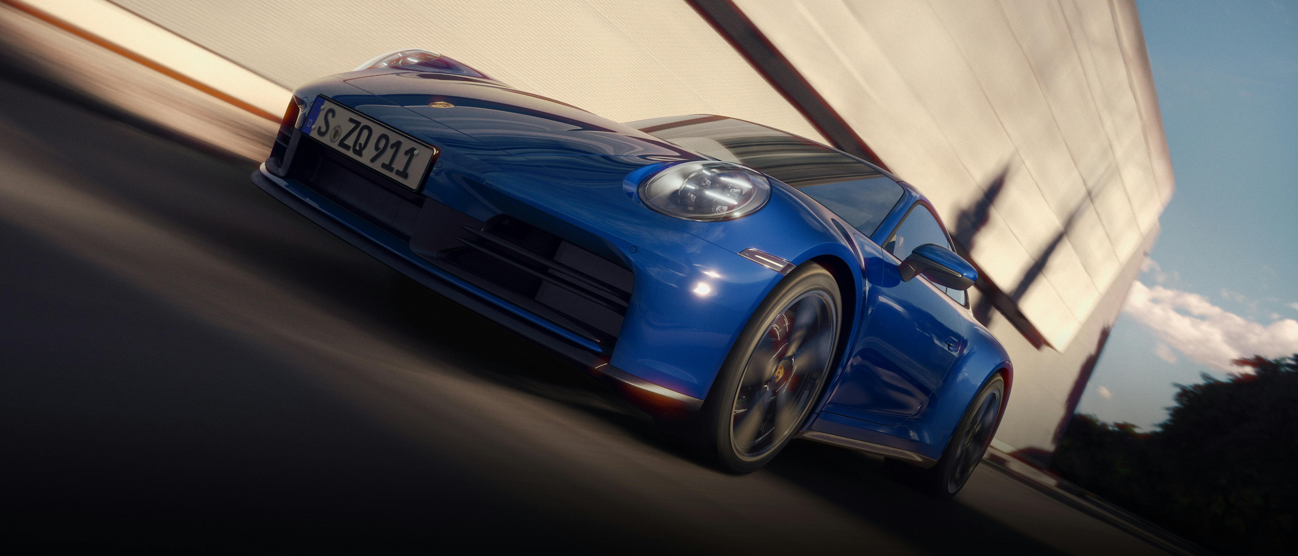 The 911 Carrera driving along a road, with white clouds in a blue sky.