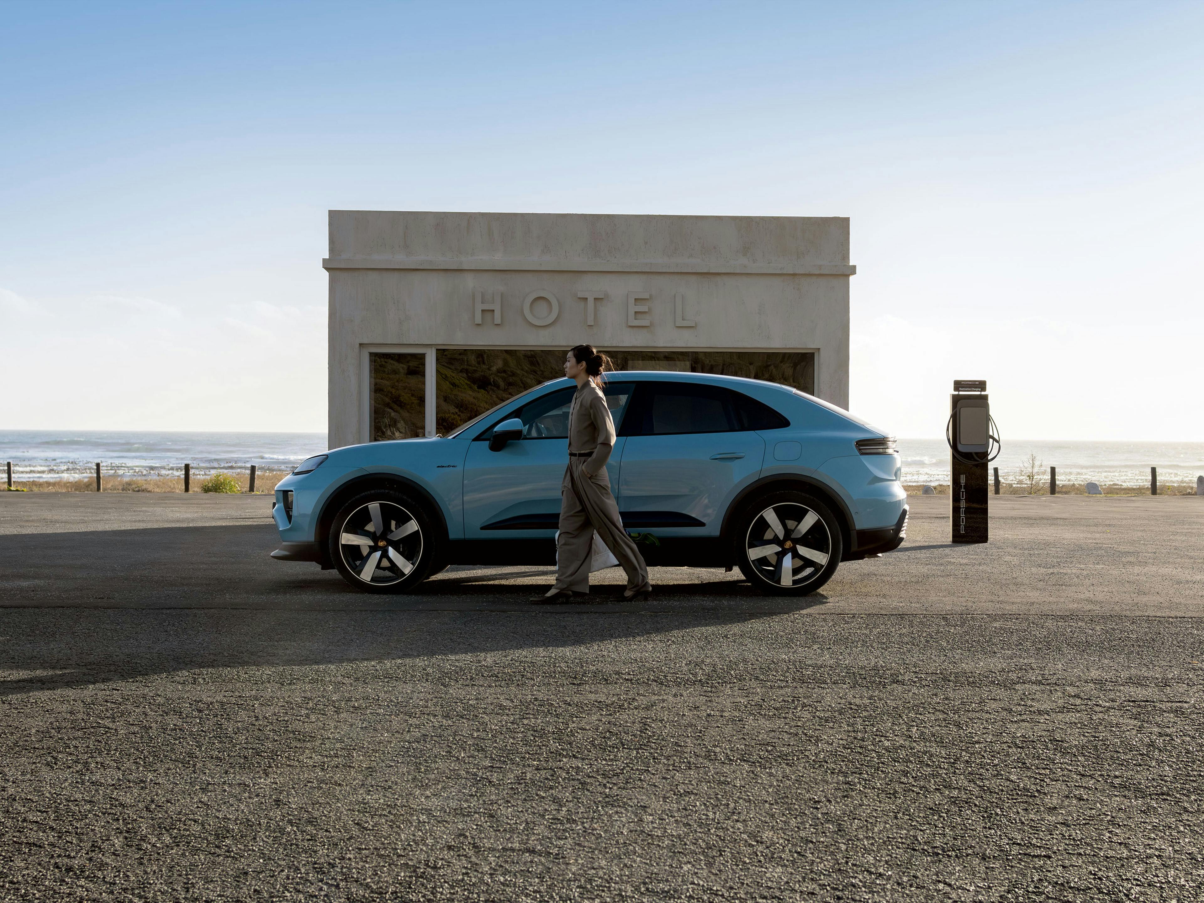 Blue Porsche Macan electric in front of hotel with charging station by the beach.