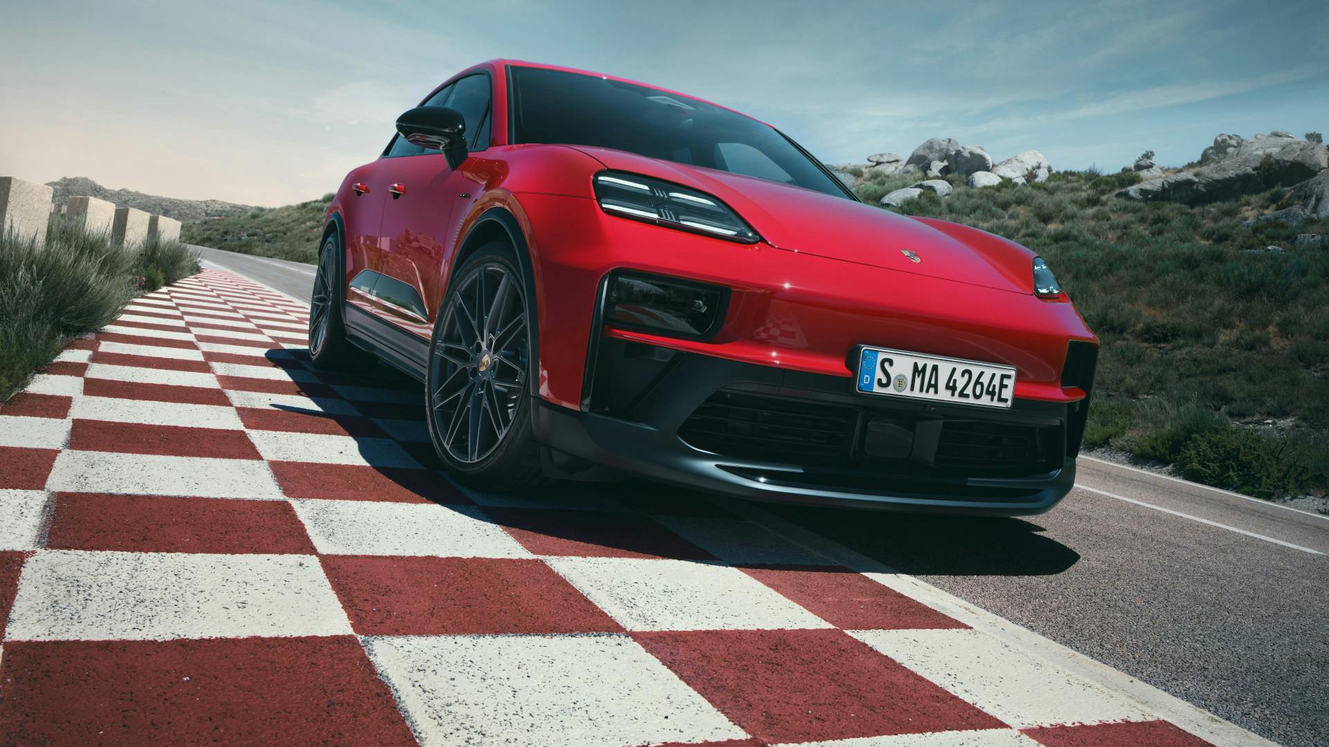 The Macan GTS Electric parked on the side of a road, where there is a red and white chequered pattern on the ground.