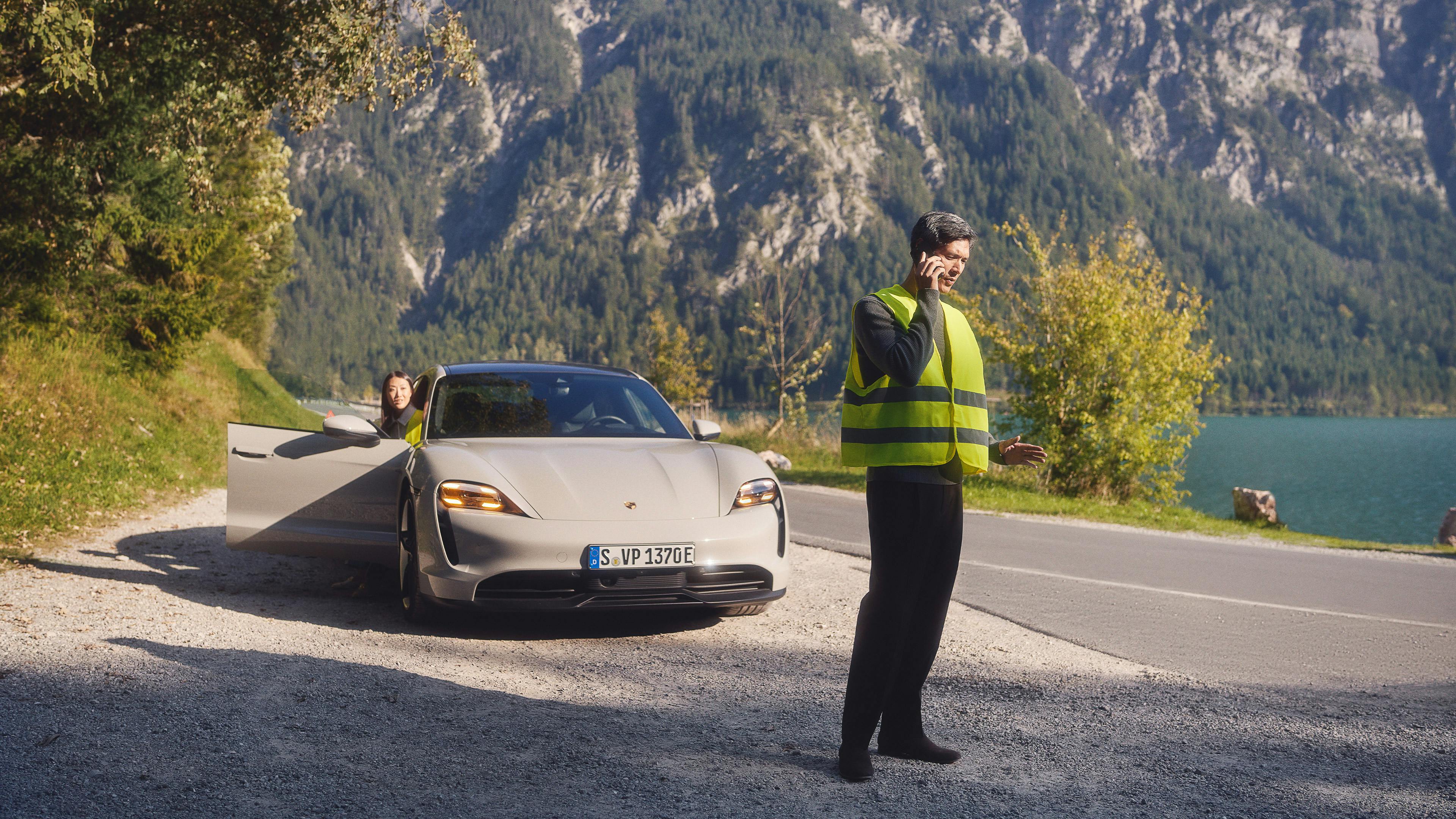 A Porsche Taycan is parked on the side of the road. A woman is getting out of the car while her husband is talking on his mobile phone in front of the car. In the interior of a Porsche, a male hand reaches towards the centre console. A bird's eye view shows a customer situation: a man and a Porsche consultant are in the Porsche showroom.