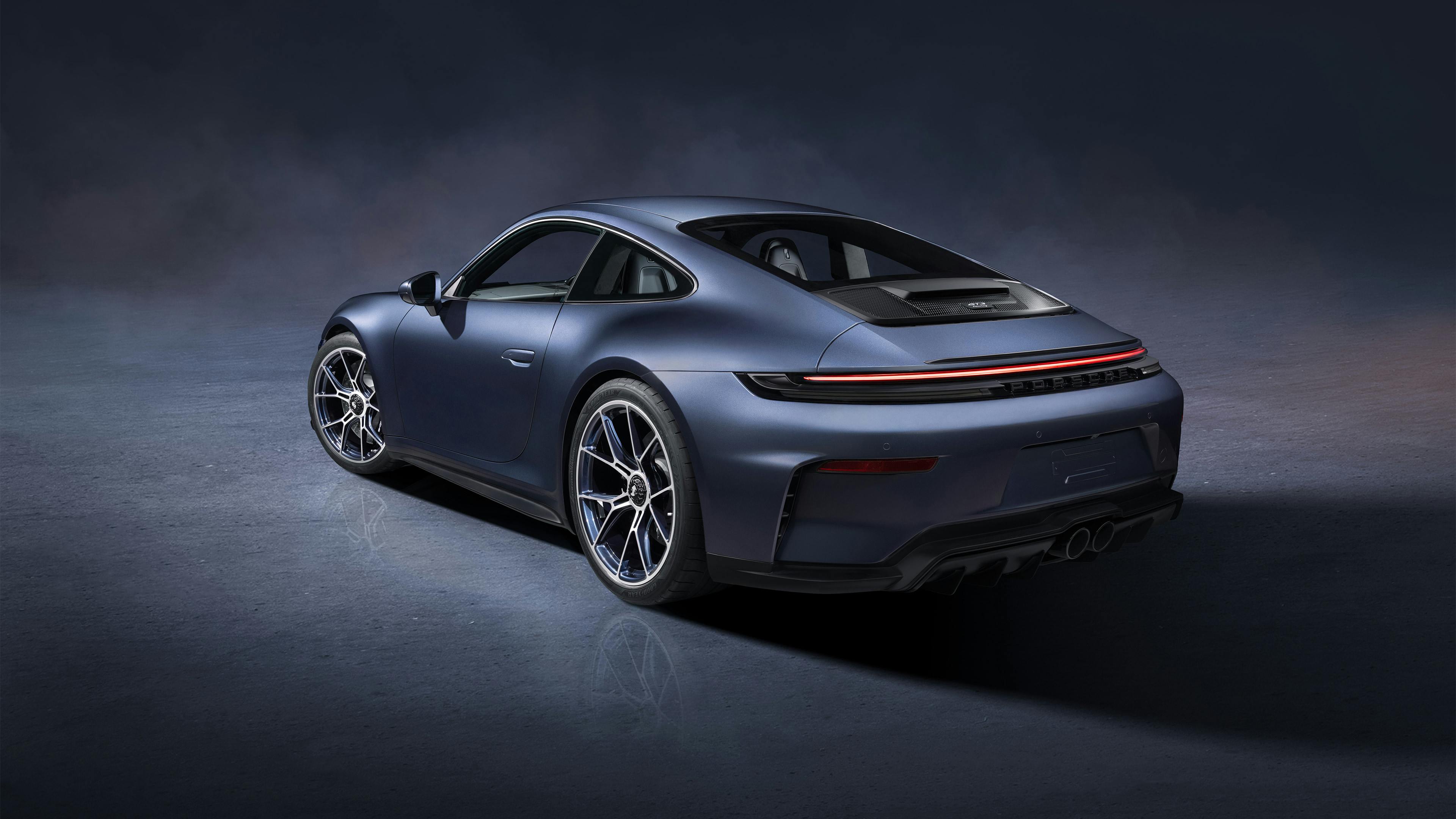 Blue-grey Porsche photographed from the rear in a studio setting, with illuminated tail light and alloy wheels.