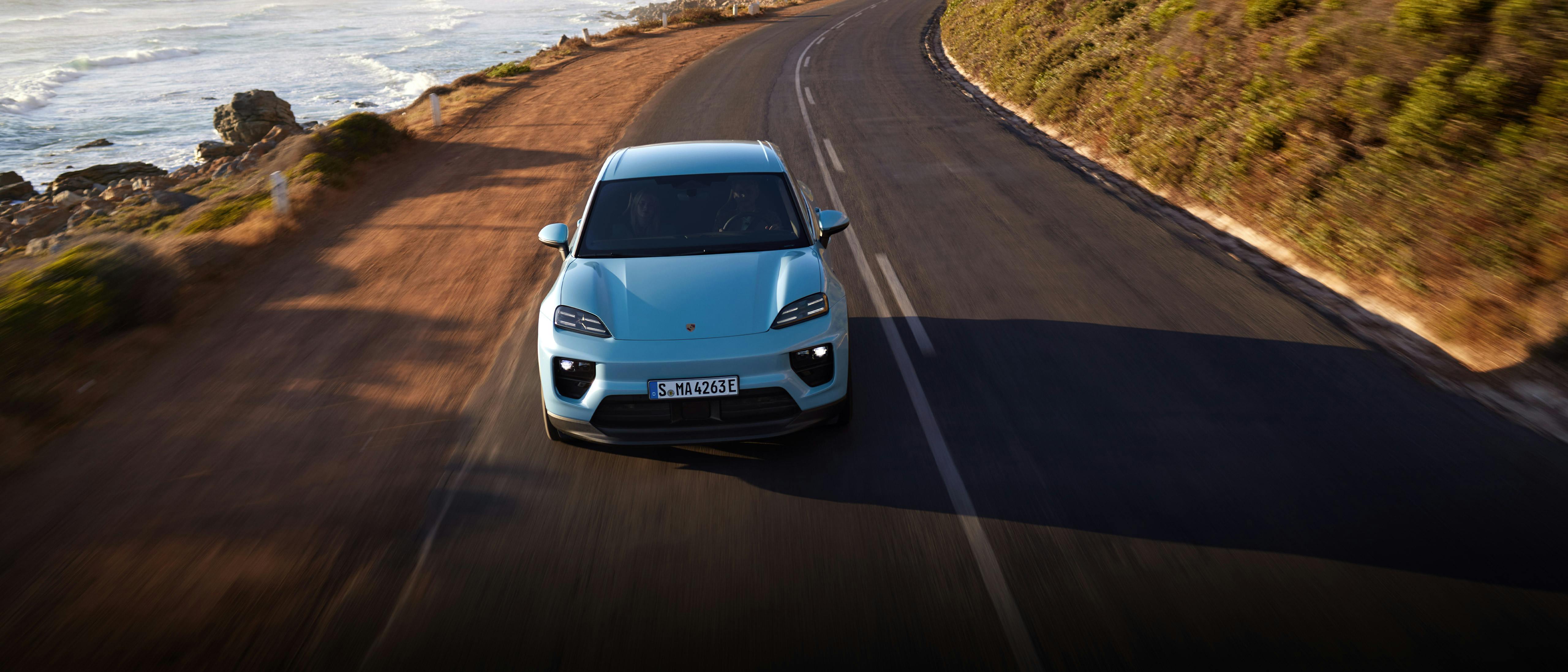 Vue avant d'une Porsche Macan bleue sur une route côtière.