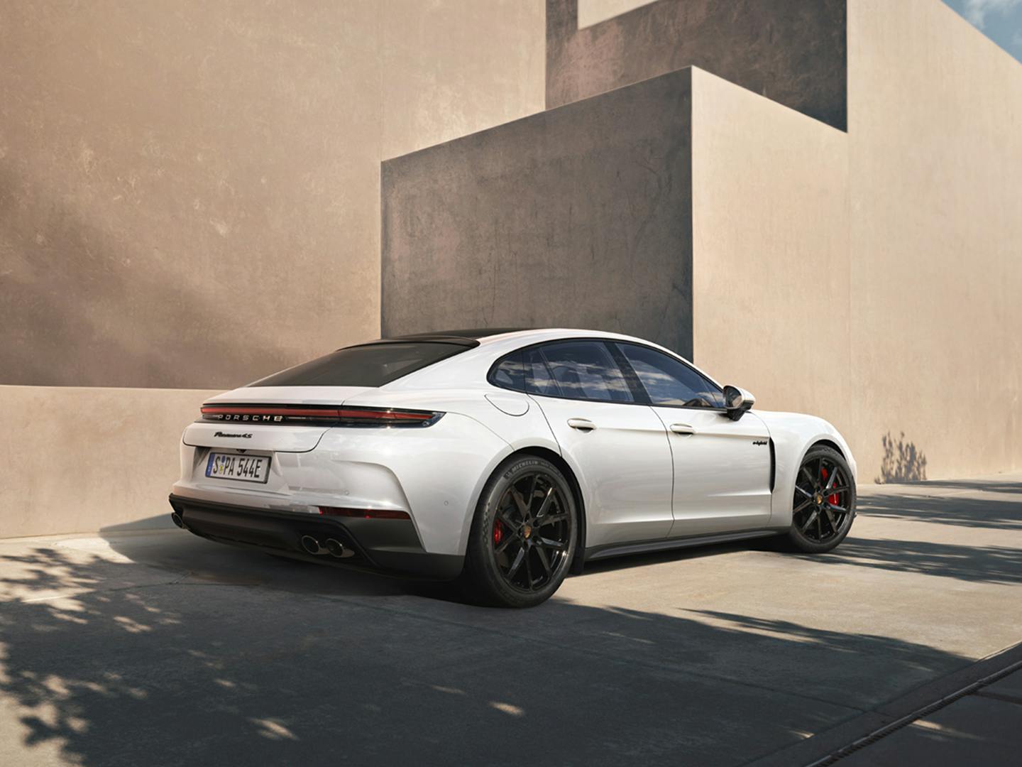 The Panamera 4S E-Hybrid parked near a stone coloured, modern building, with the shadows of a nearby tree in the foreground.