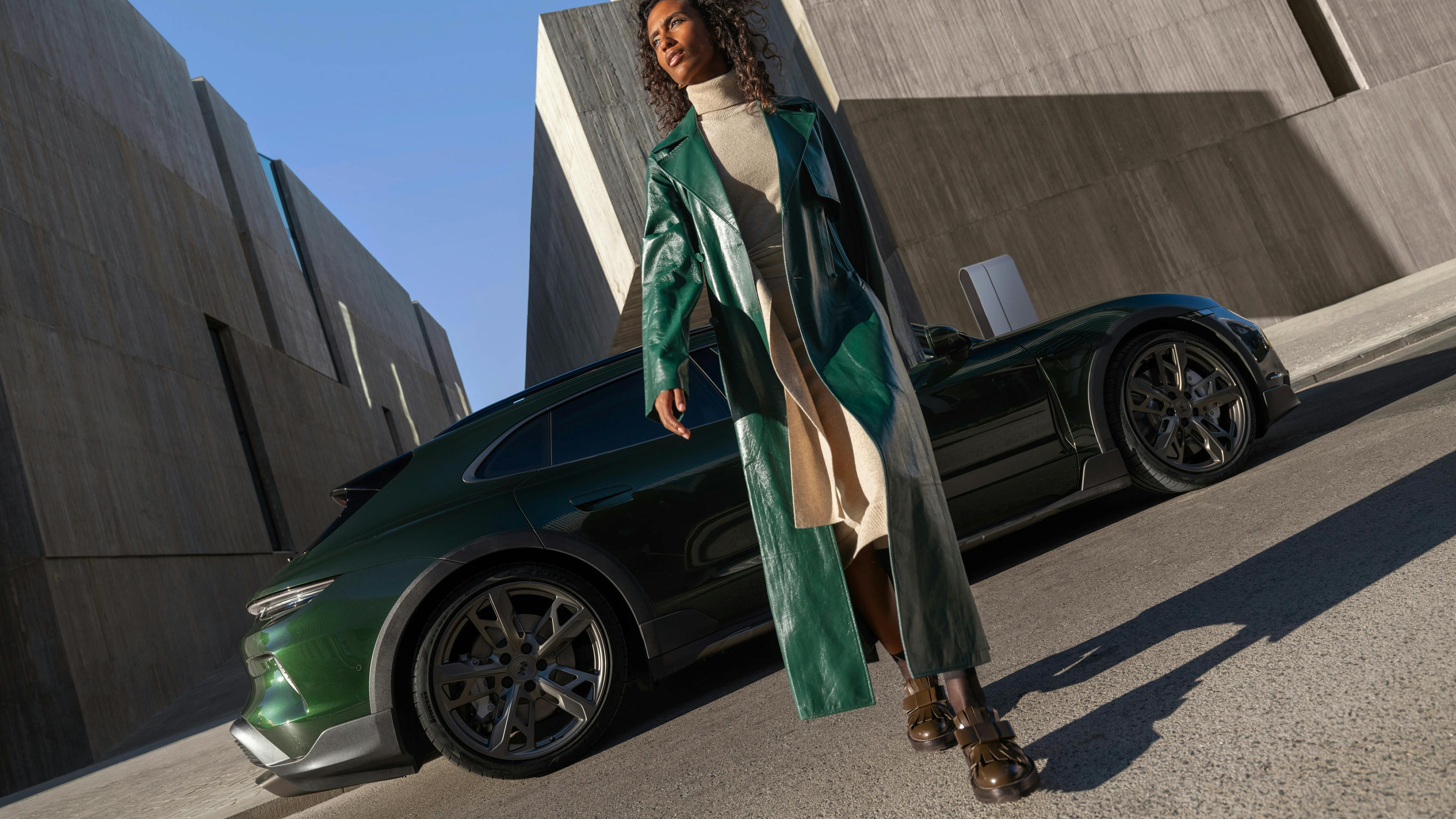 A Porsche Taycan Turbo Cross Turismo in front of a villa next to a Wallbox. A woman plugging in the plug.