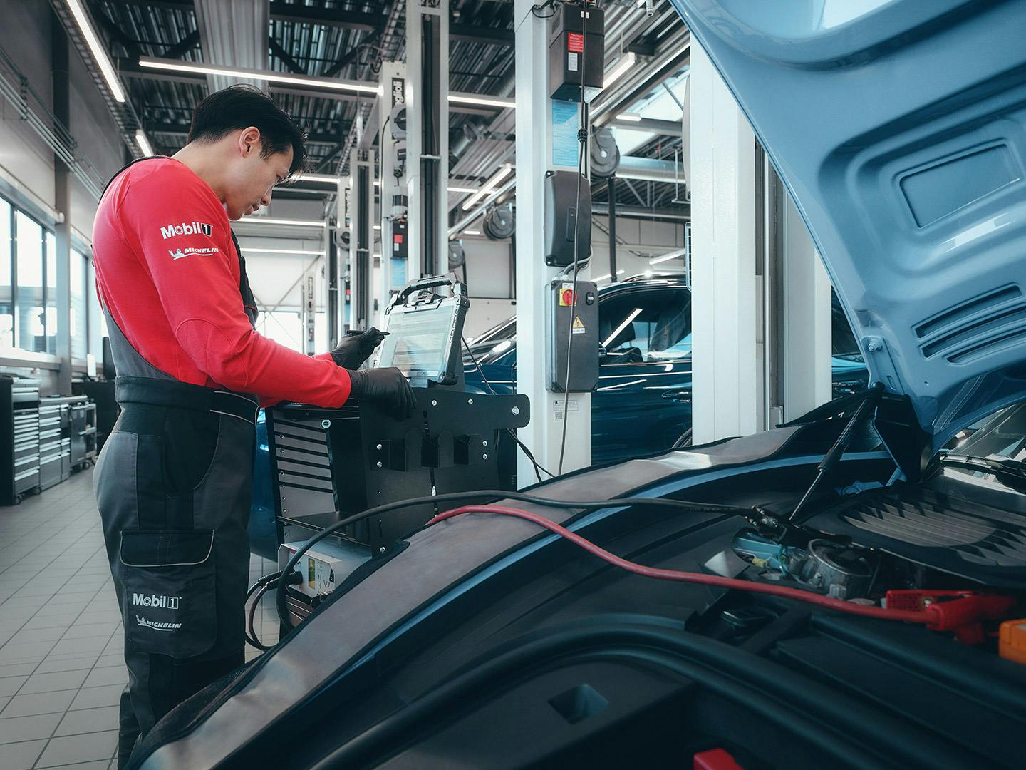 A workshop employee leaning over the open bonnet of the Taycan and using the diagnosis tester on the vehicle.