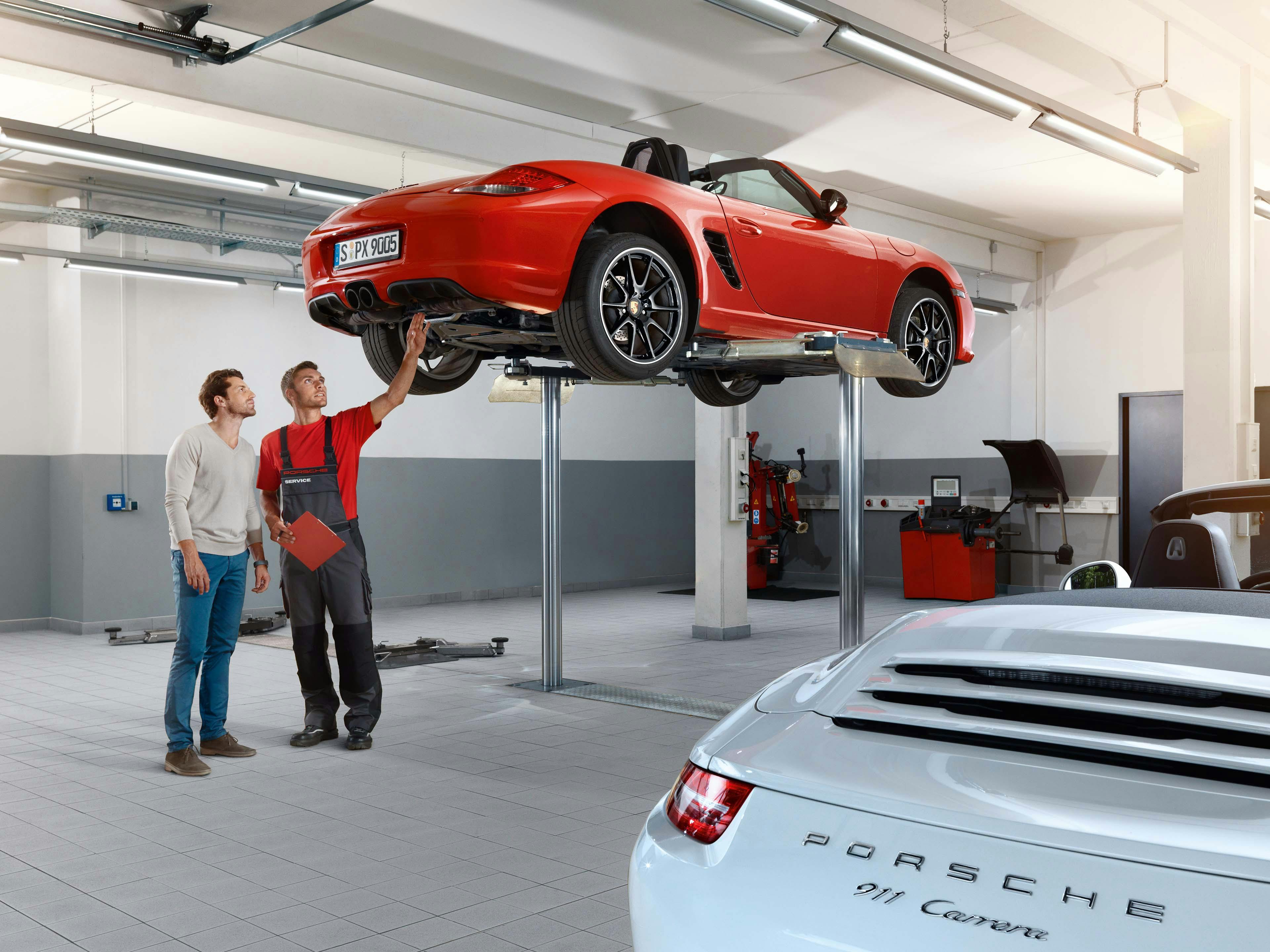 Een werkplaats met een monteur die iets aan een Porsche aan een klant laat zien.