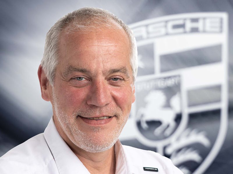Een man in profiel, die contact persoon is voor Porsche Classics, met een Porsche logo op de achtergrond