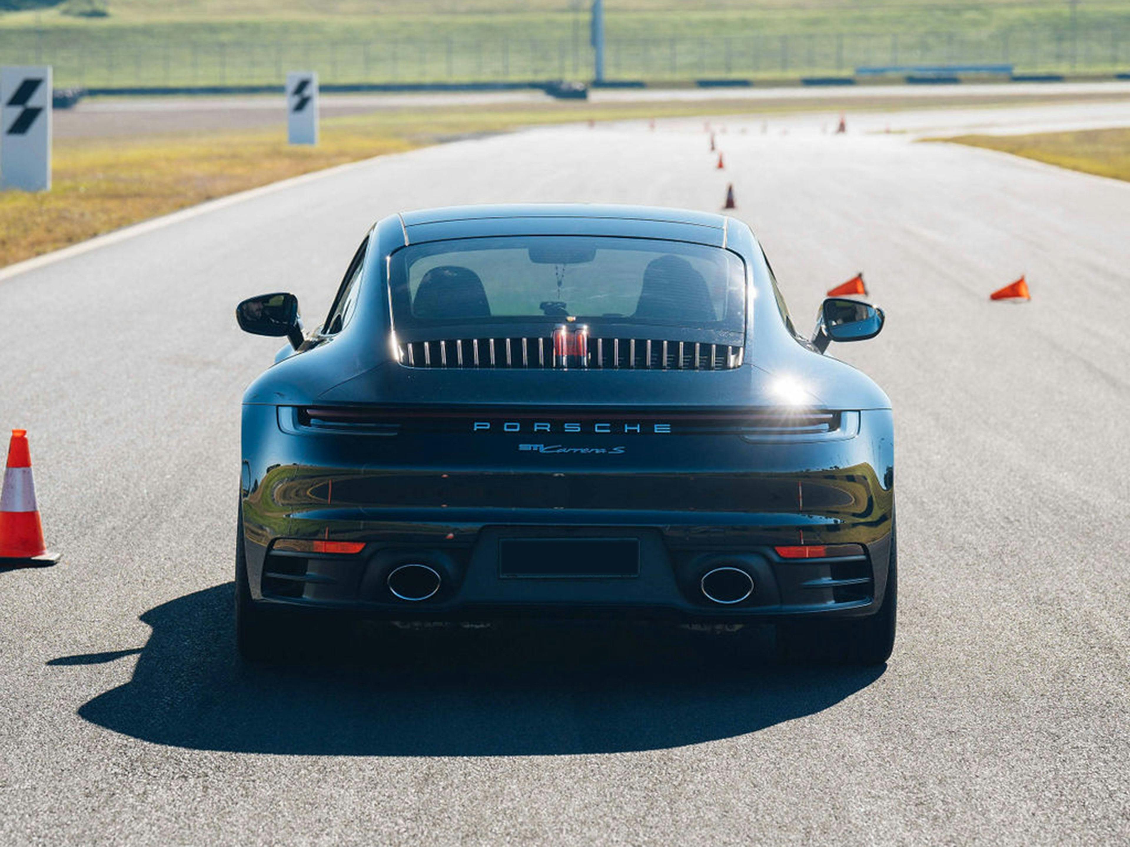 Black Porsche parked on a racetrack with safety cones ahead.