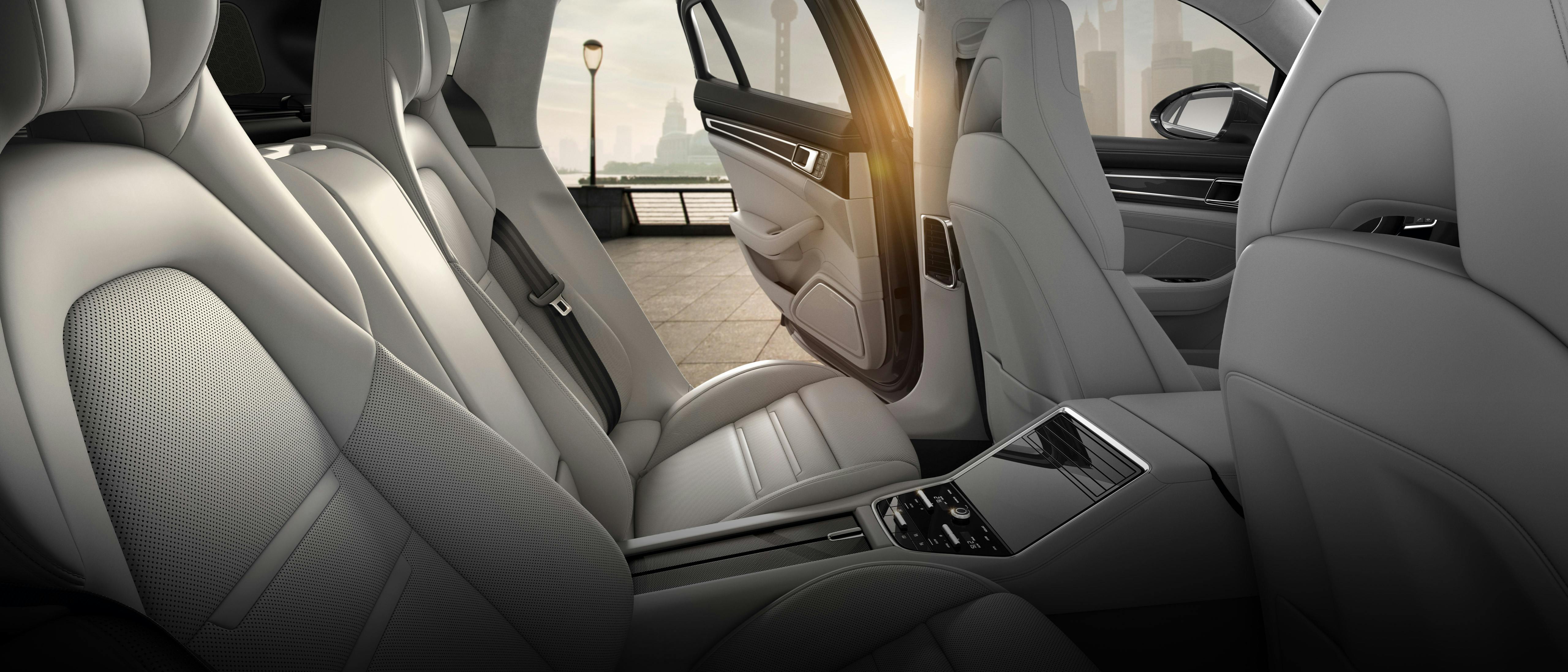 Die hintere Sitzreihe eines Porsche mit weißen Ledersitzen, einem Panoramadach und einer Mittelkonsole mit Touchscreen.