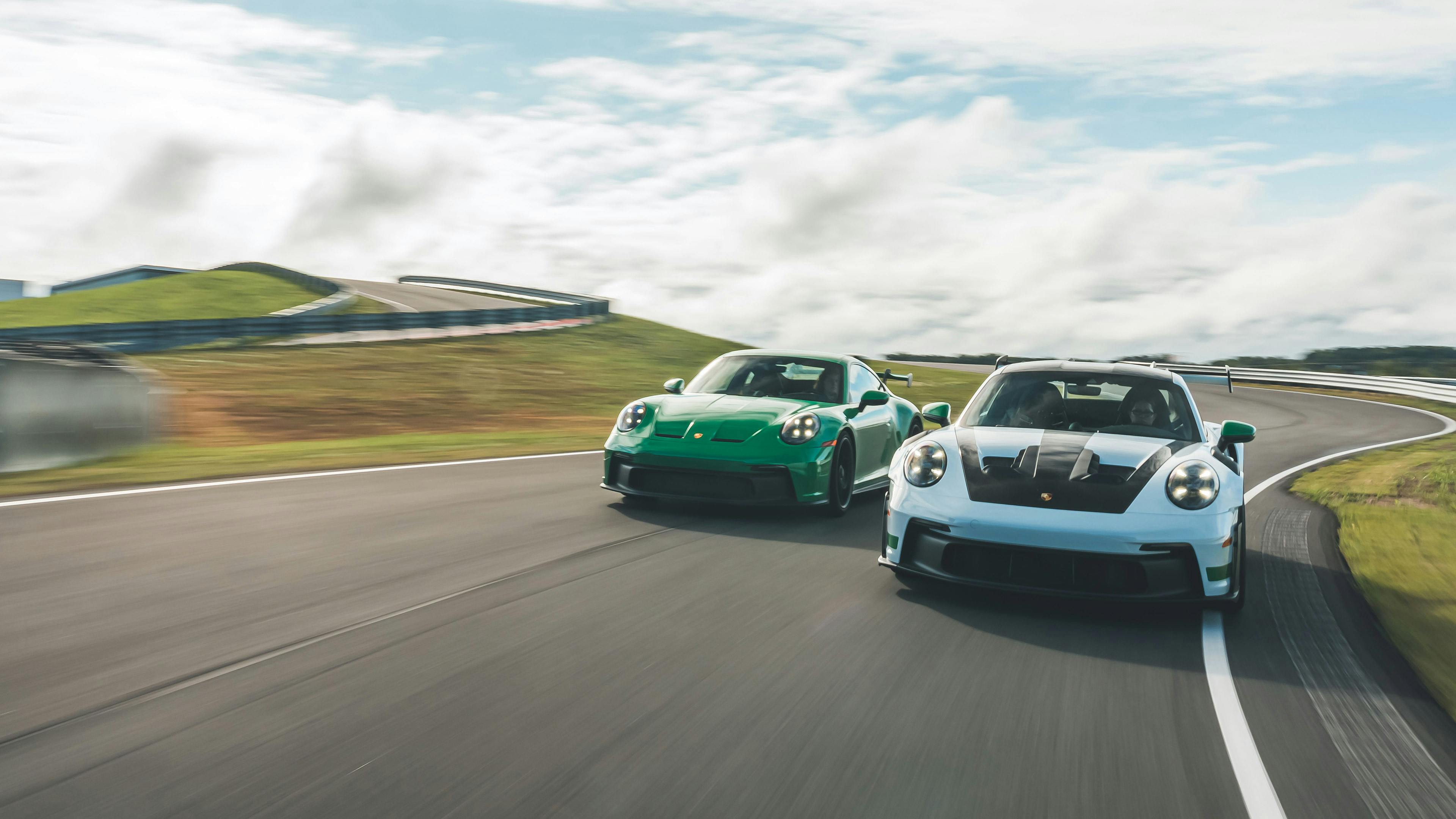 Two Porsche 911 GT3 RS models driving side-by-side on a racetrack.
