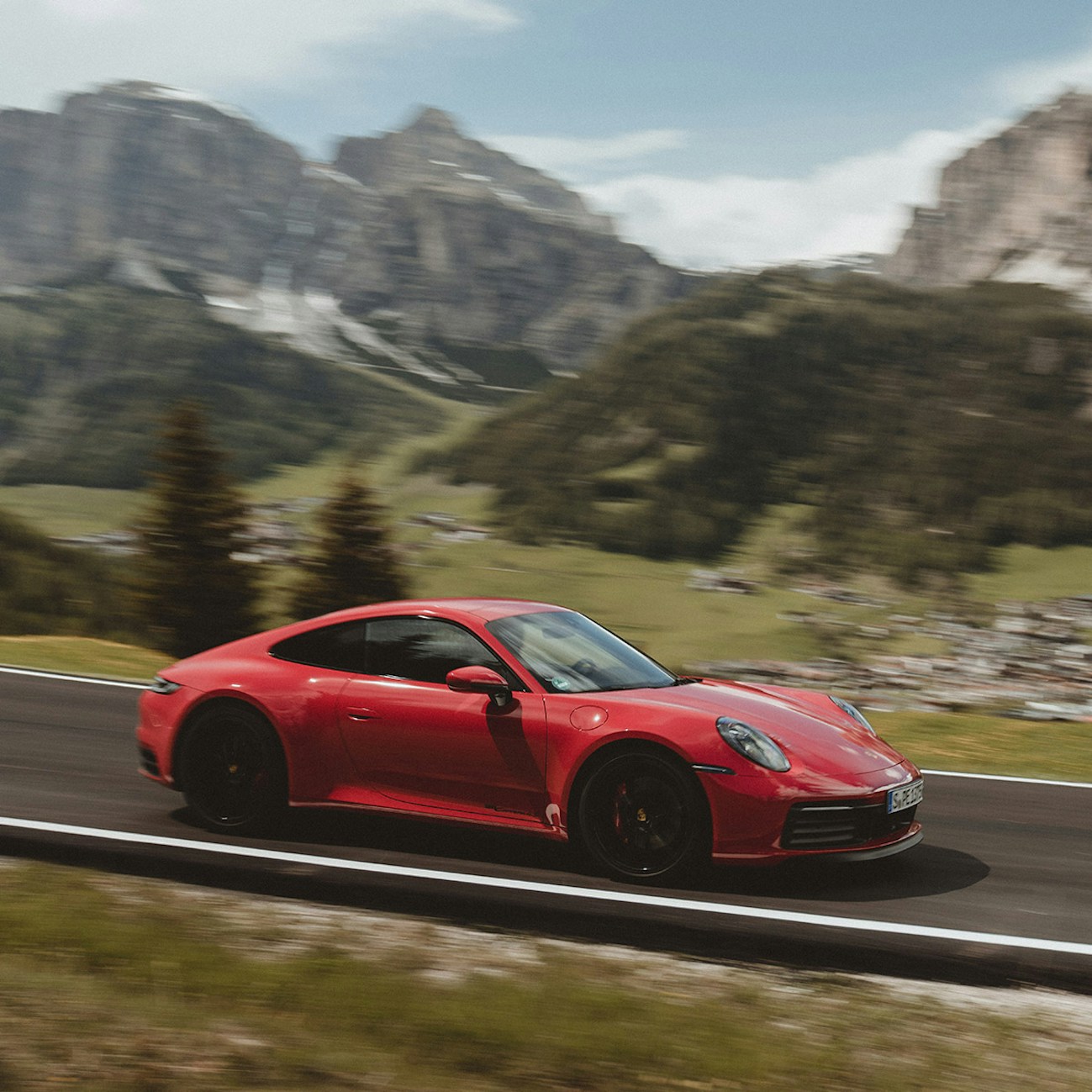 Macchina Porsche rossa che guida lungo la strada nelle Alpi.