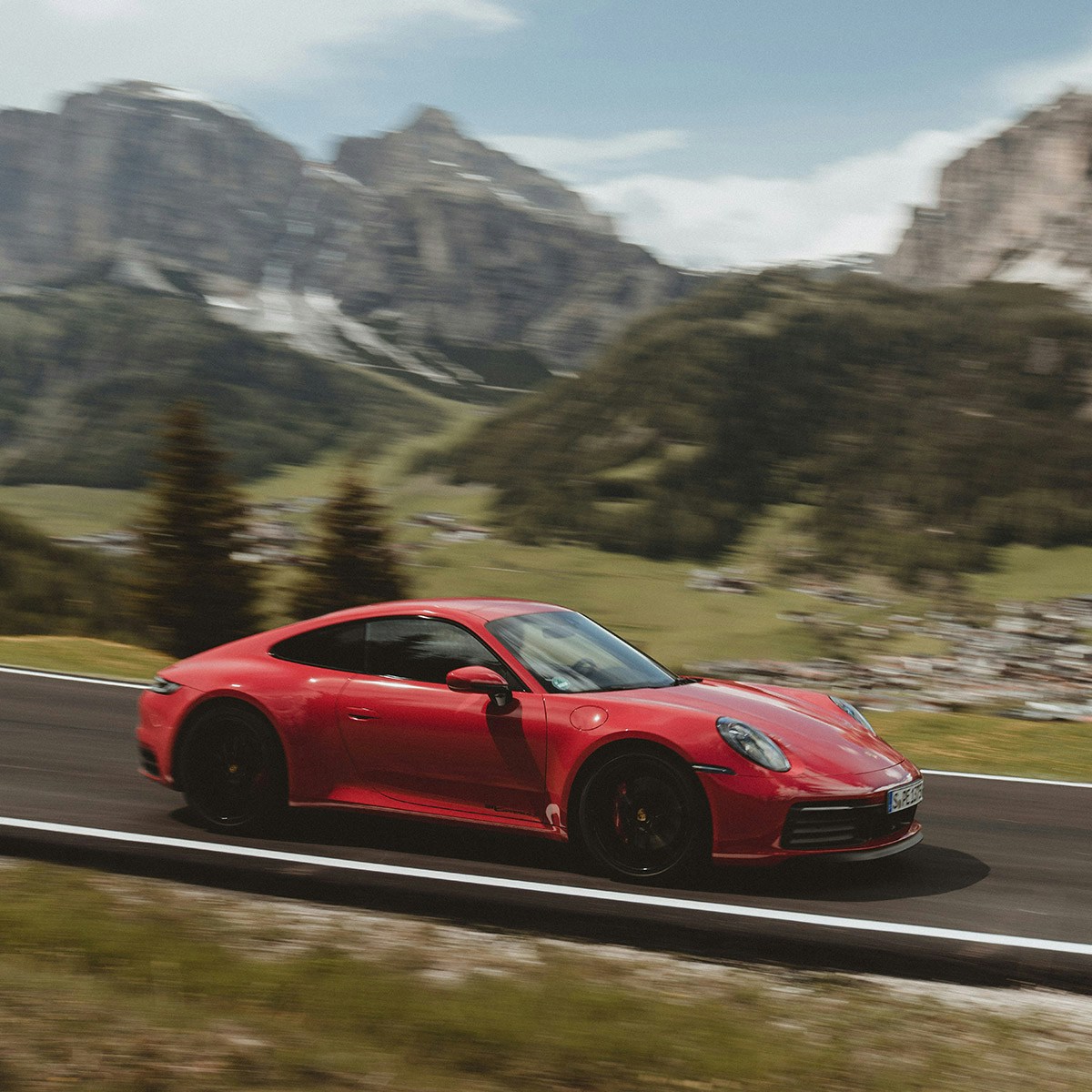 Ein roter Porsche fährt eine Strasse in den Alpen entlang.