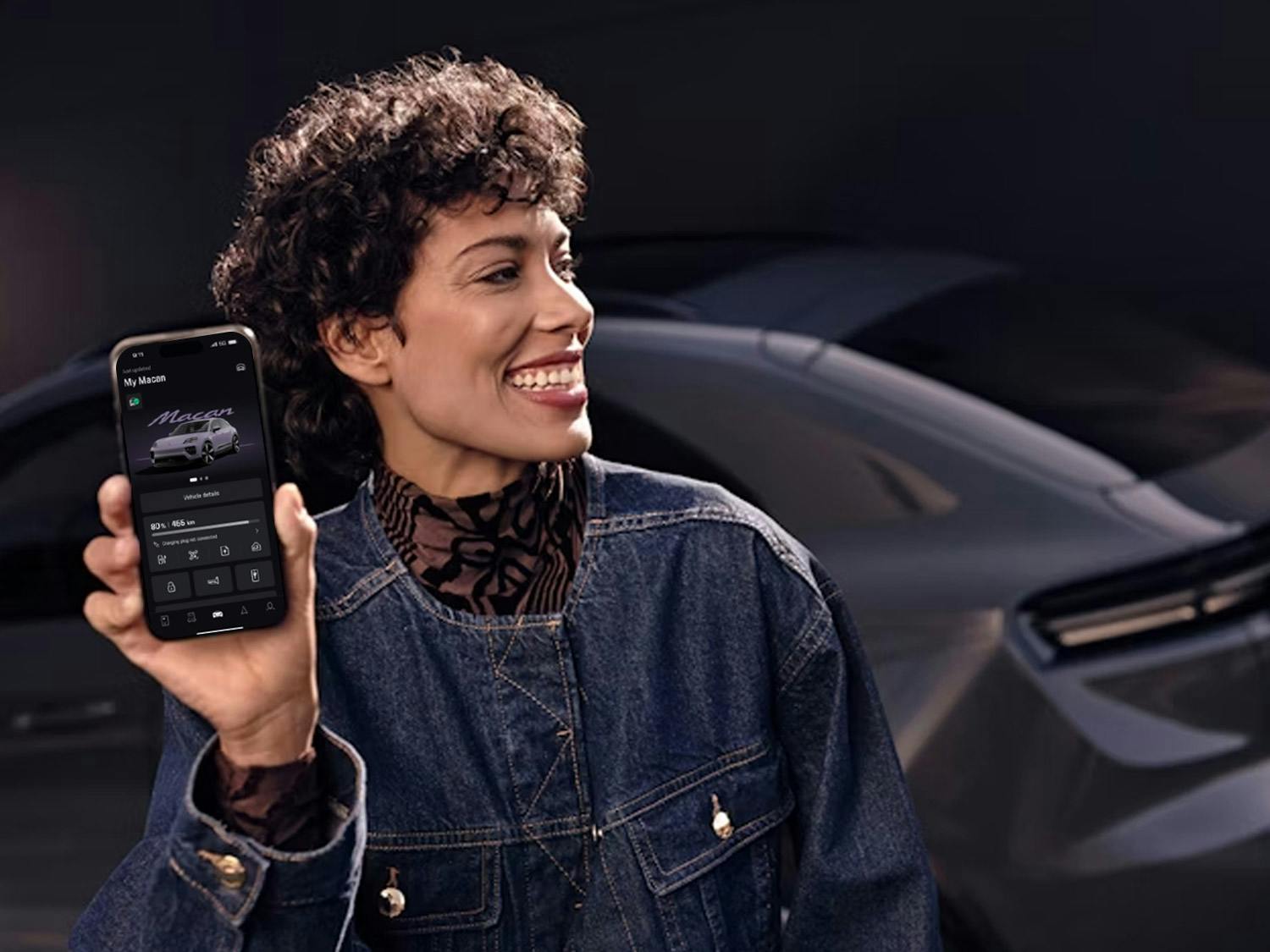 A smiling woman holds her smartphone with the My Porsche app open up to the camera.