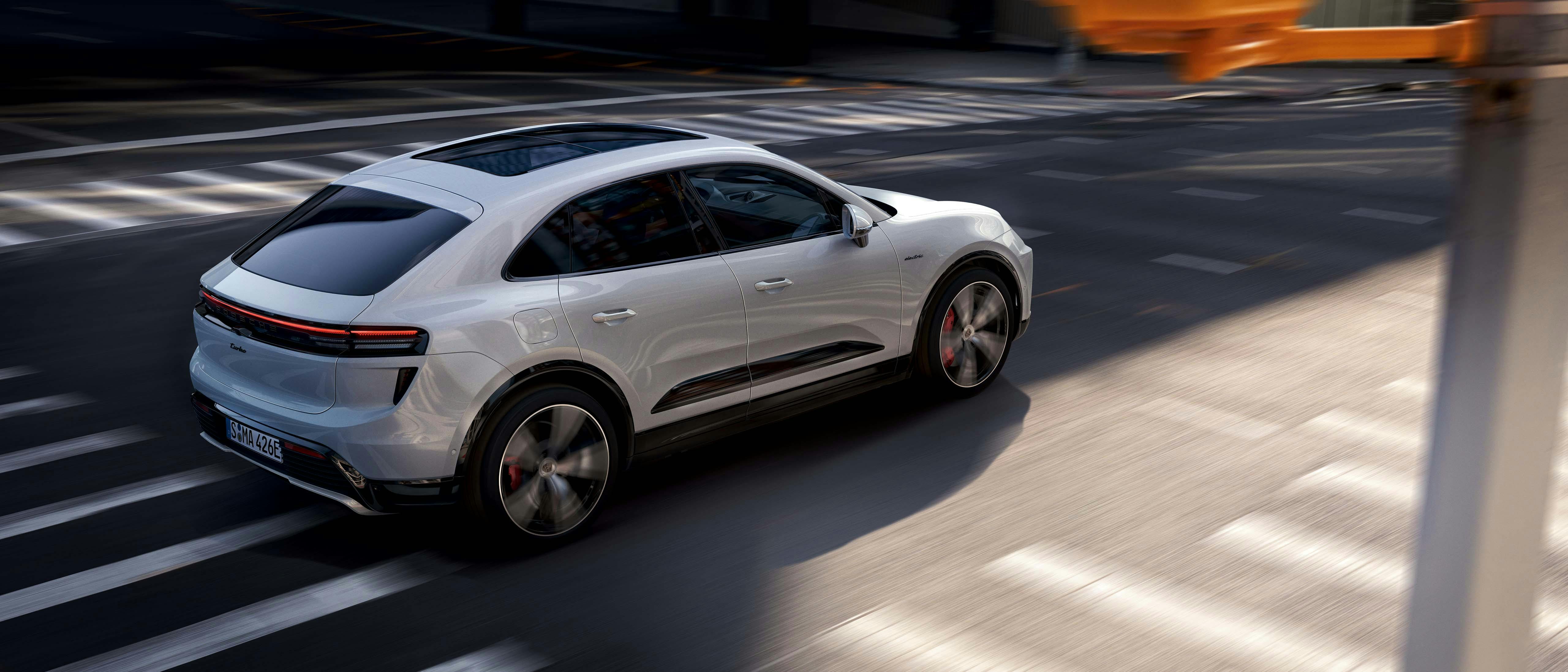 Witte Porsche Macan elektrisch aan het rijden in de stad, rondom liggen zebrapaden.