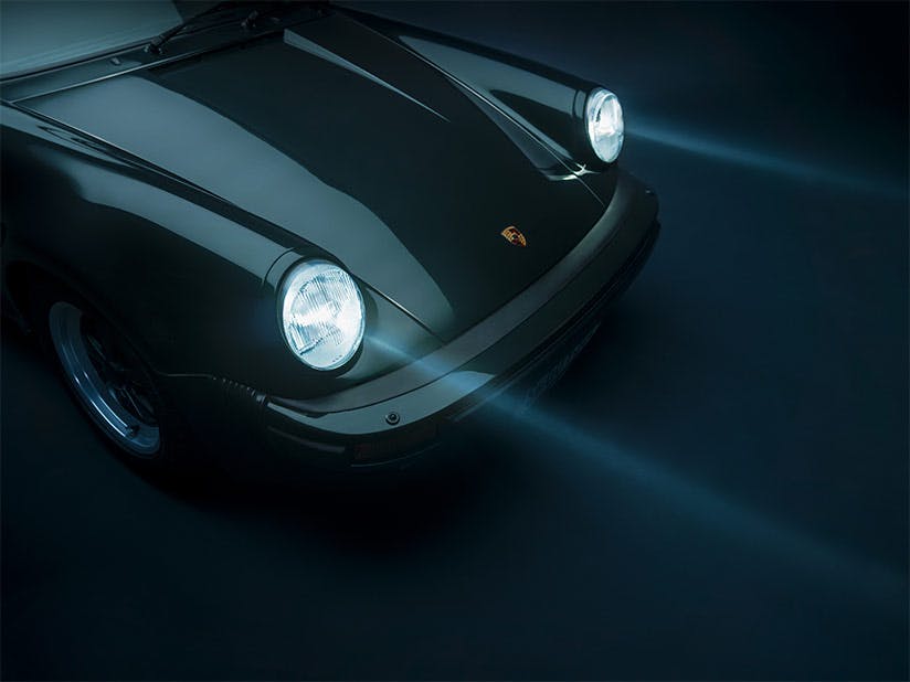 Front view of a classic 911 with headlights turned on, shining beams of light in a dark environment.