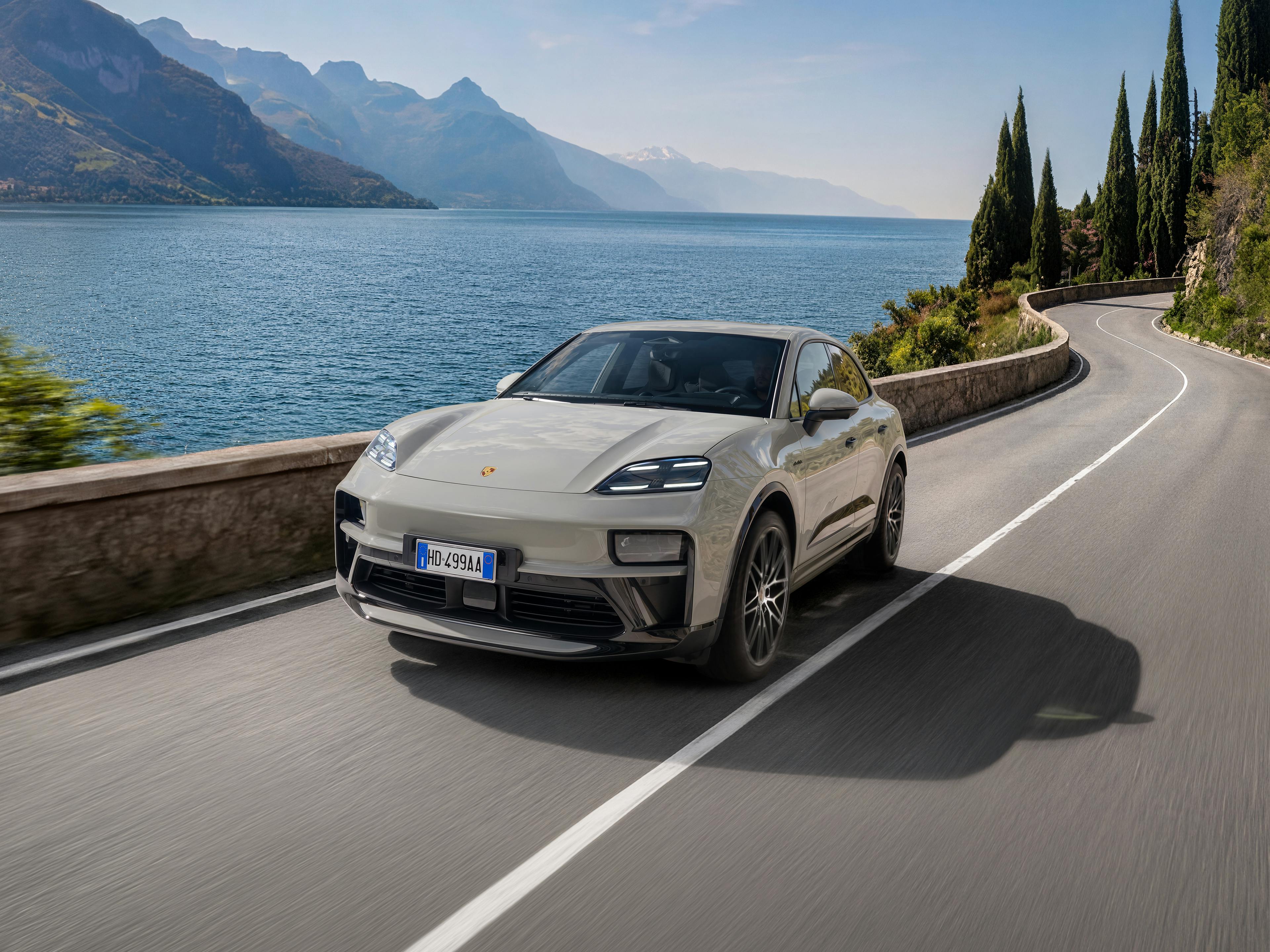 Porsche Macan e-motion percorre una strada asfaltata con un lago sullo sfondo.