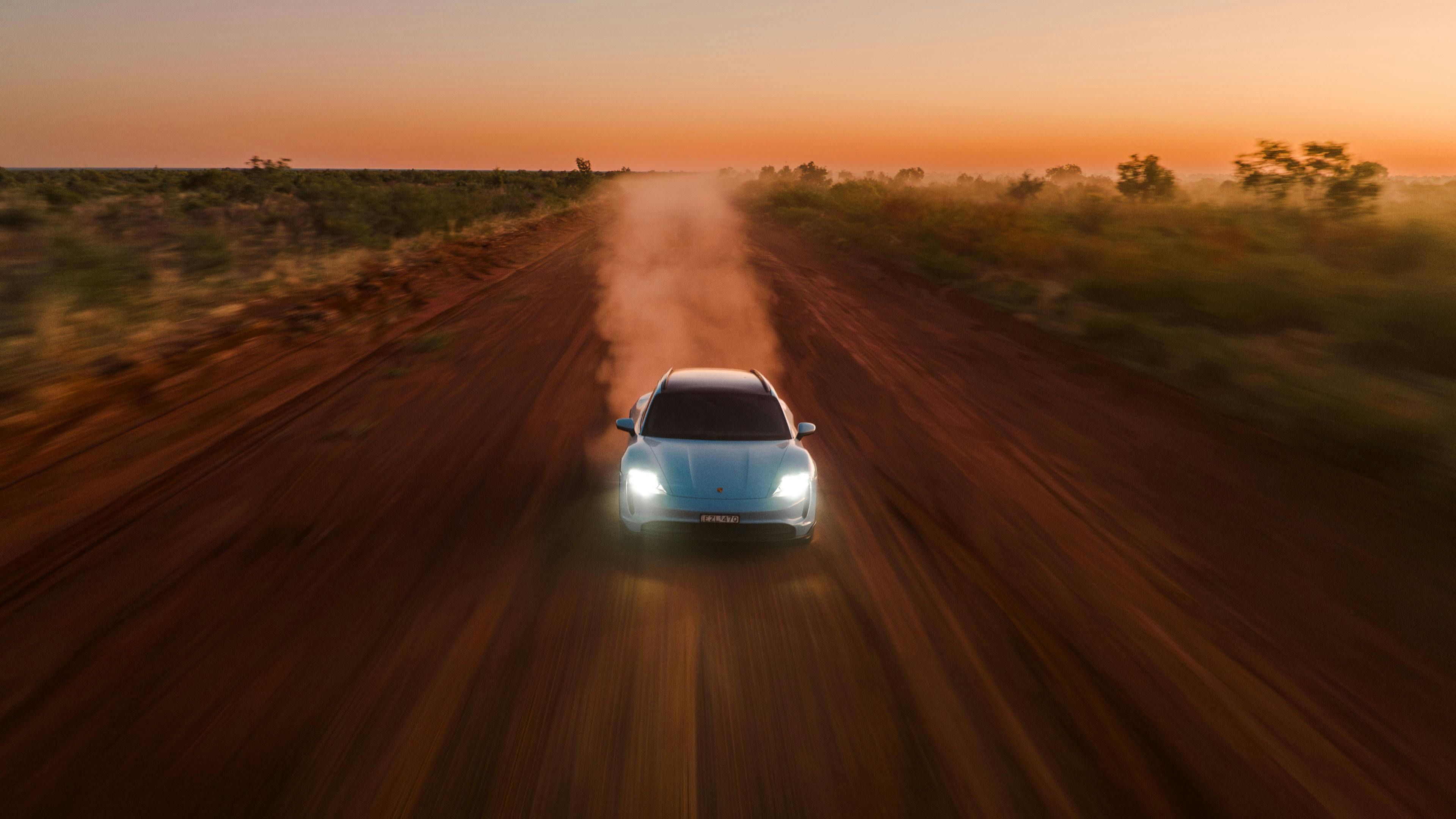 Porsche Taycan driving on a picturesque desert landscape with dust trailing
