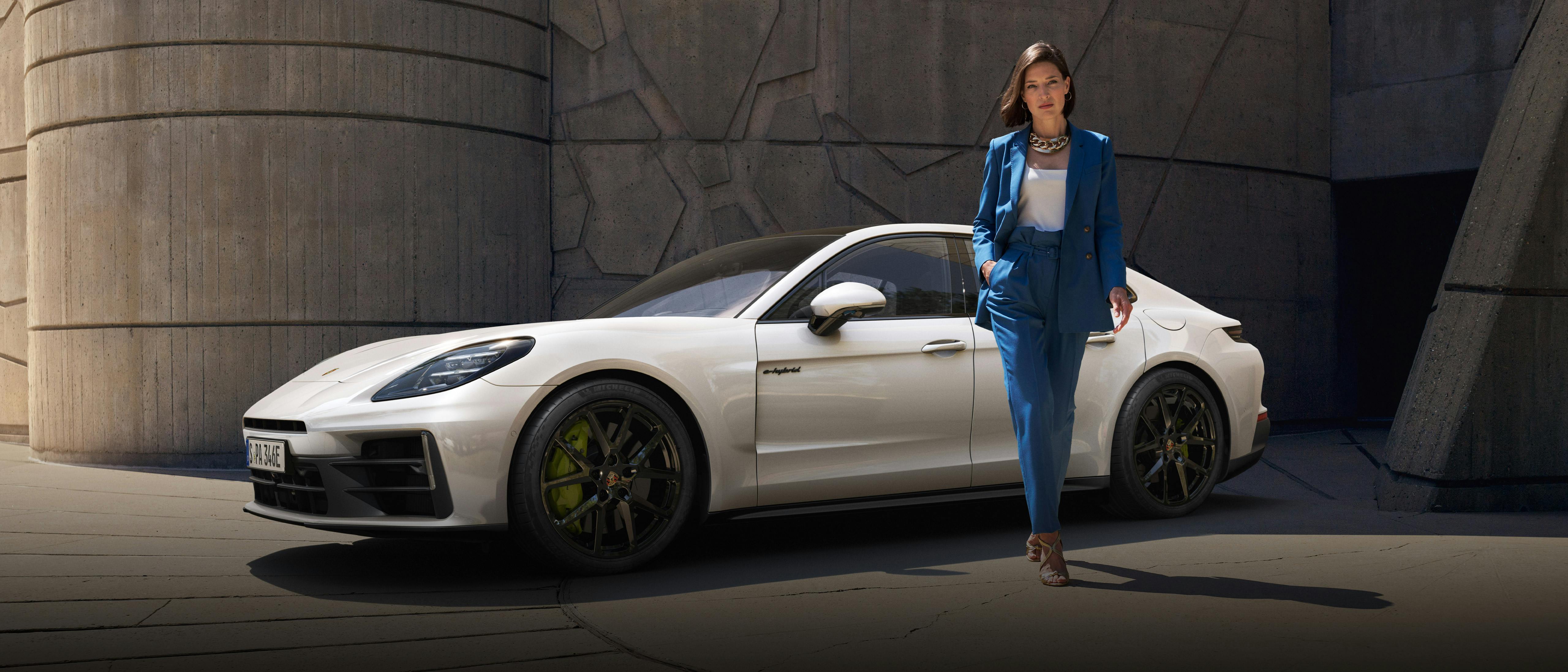 The Panamera 4 E-Hybrid parked near a stone building, with a woman walking away from the car.