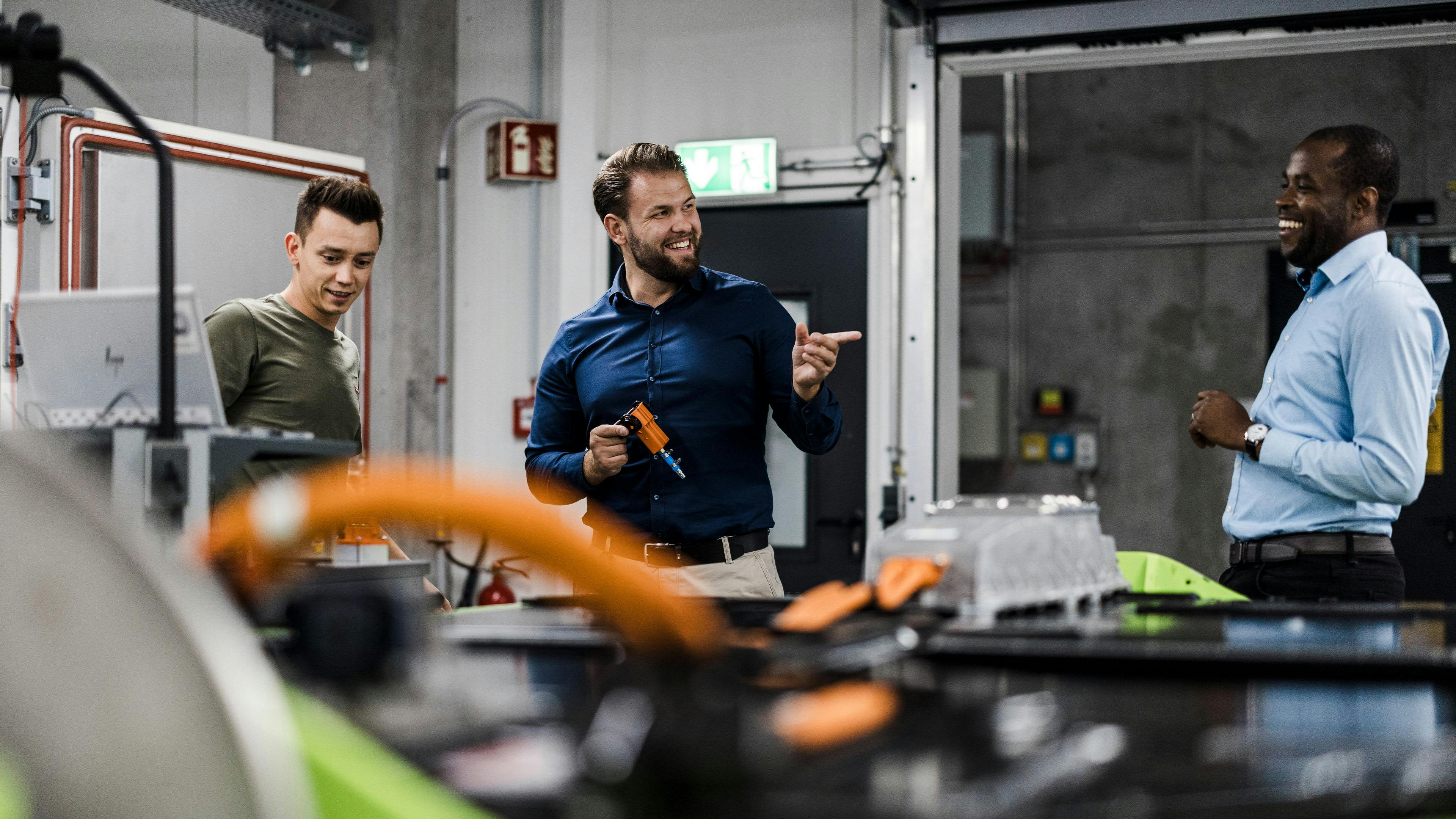 Drei Porsche Entwicklungsingenieure haben Spaß in der Werkstatt bei der Diagnose eines Fahrzeugs.