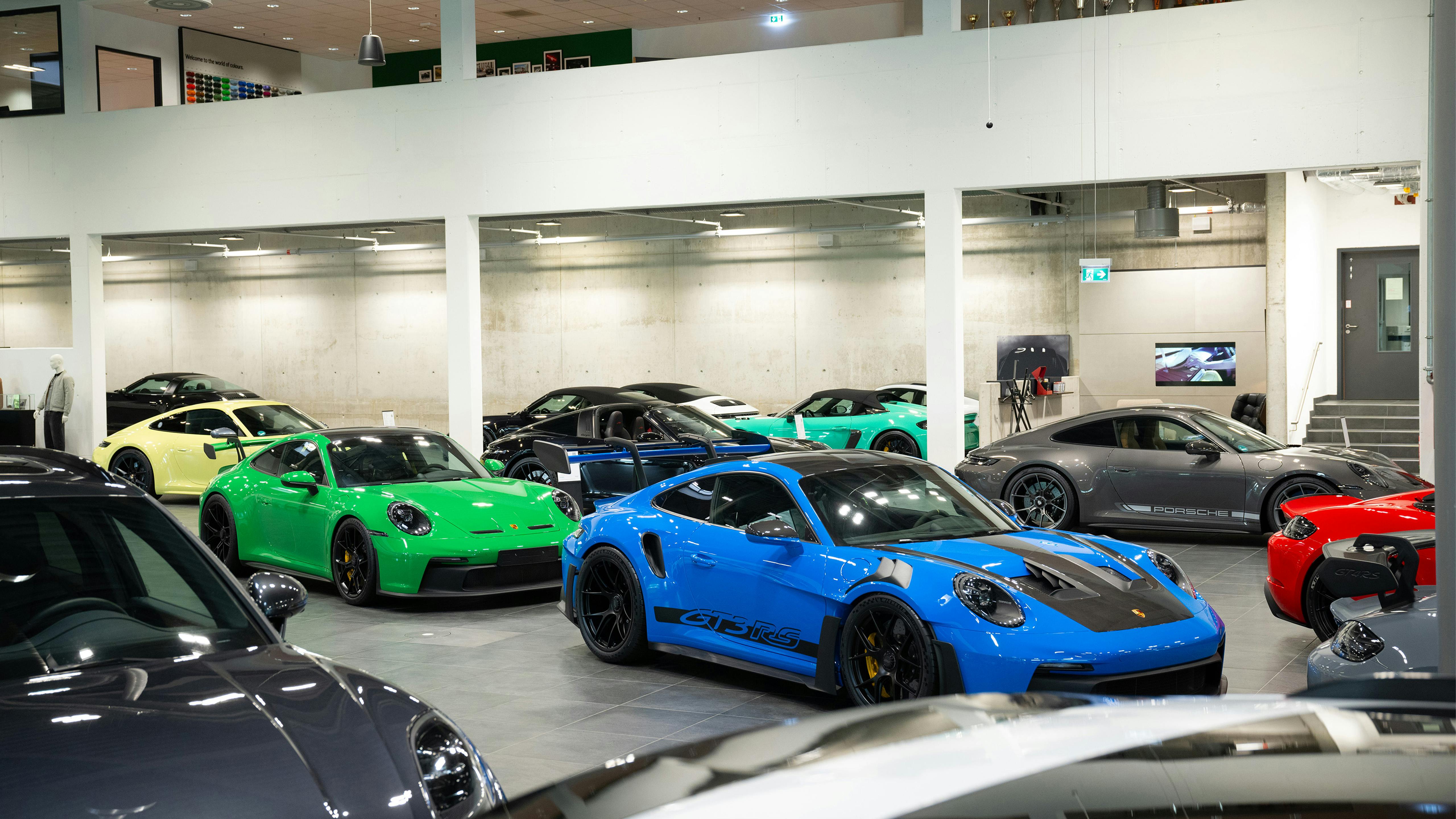 Blauer Porsche GT3 RS im Vordergrund vor grünen, gelben, türkisen und grauen Modellen im Showroom.