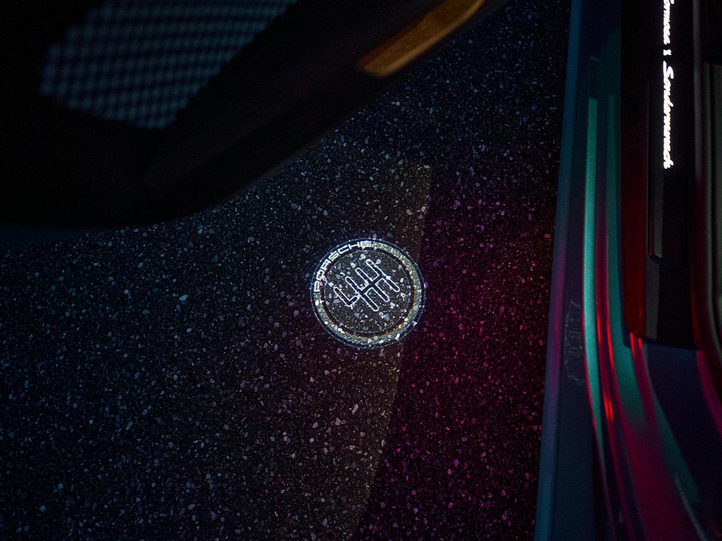 Detail of a Porsche 911 Carrera door area showing illuminated projection of gear shift pattern on dark asphalt.