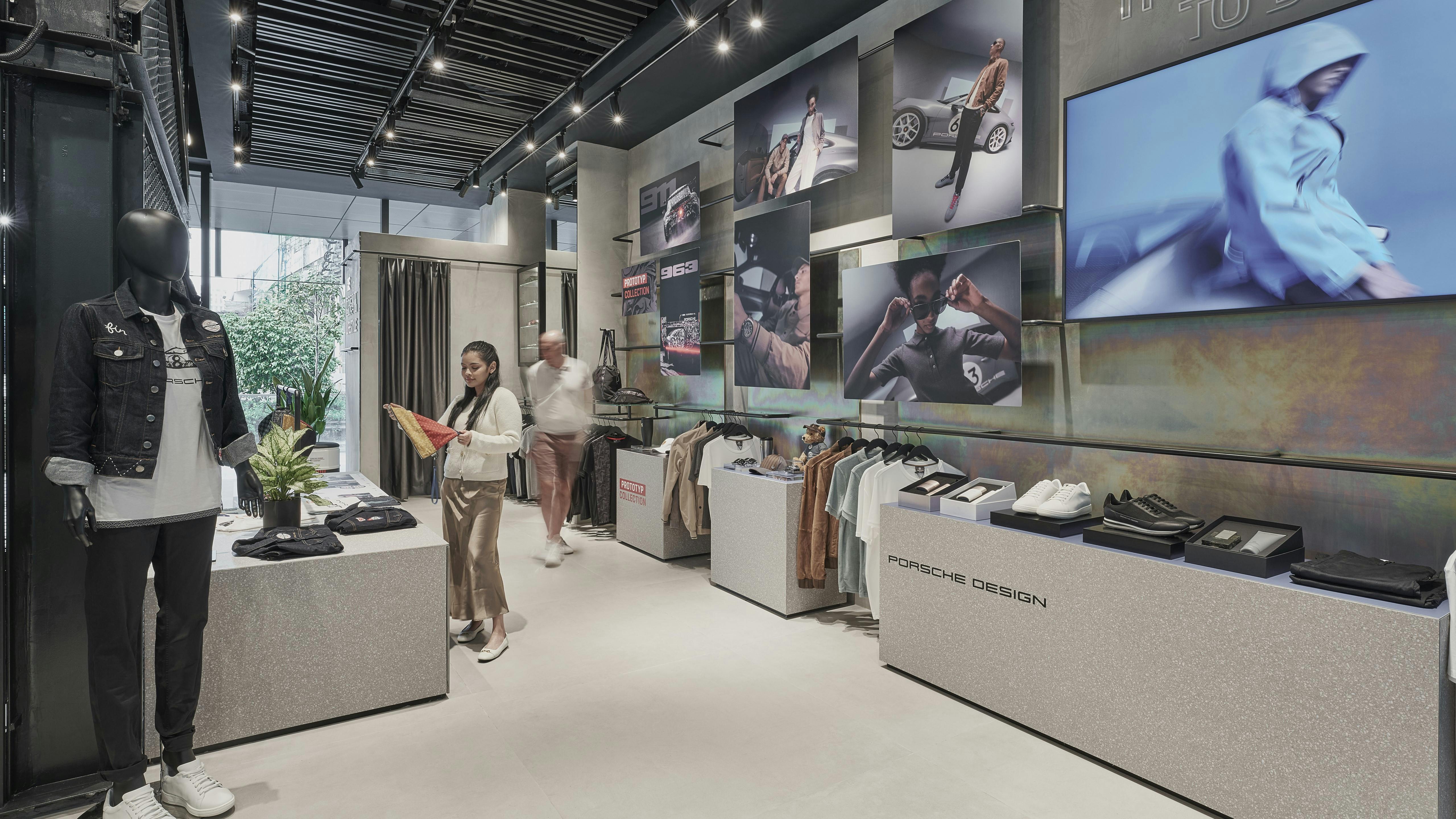 Two customers browsing Porsche Lifestyle merchandise at Porsche Studio Singapore, with Porsche Design items displayed on shelves.