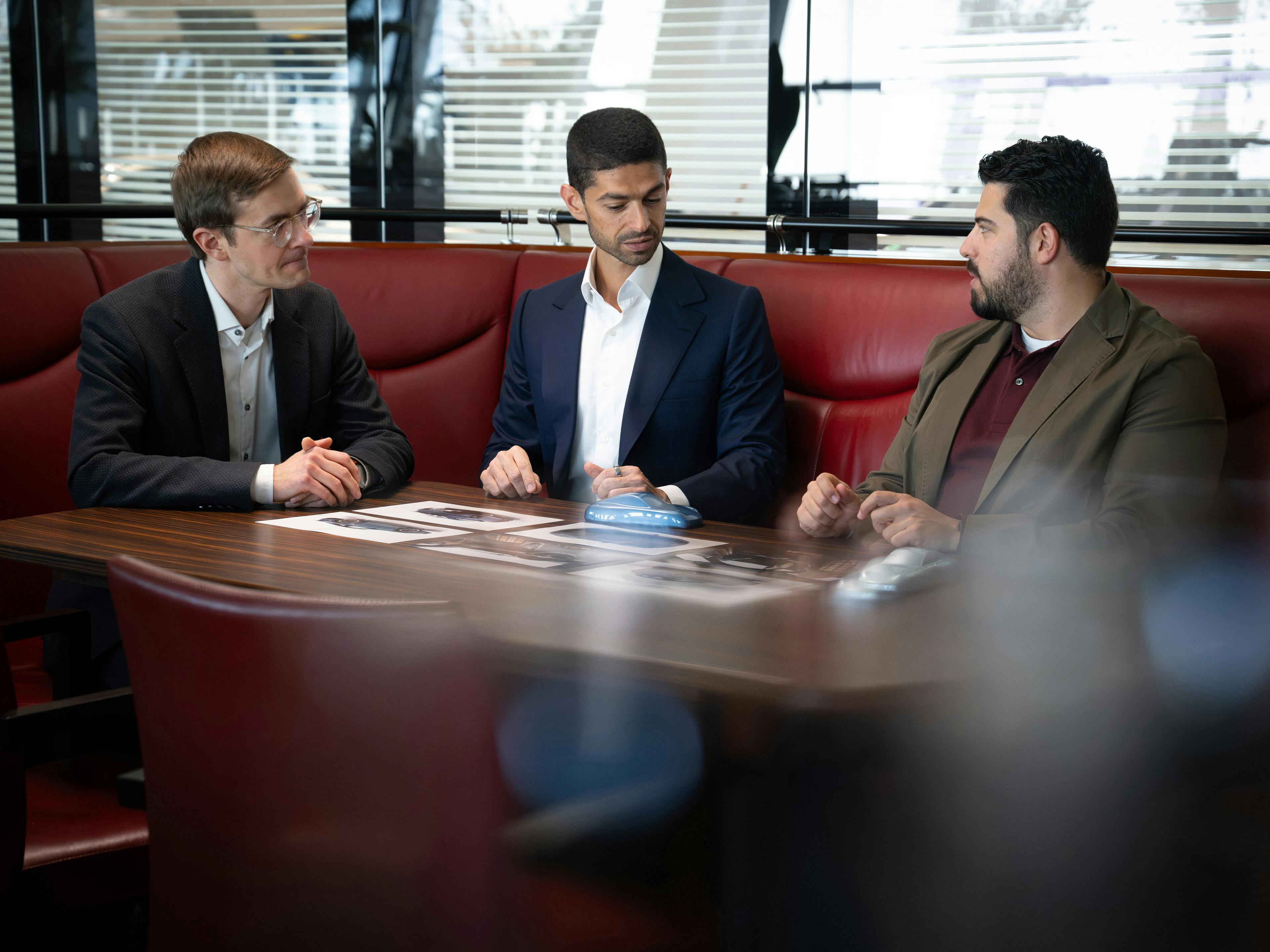 Drie mannen zijn bezig met een overlegvergadering bij Sonderwunsch Manufaktur, zittend rond een tafel met documenten voor zich.