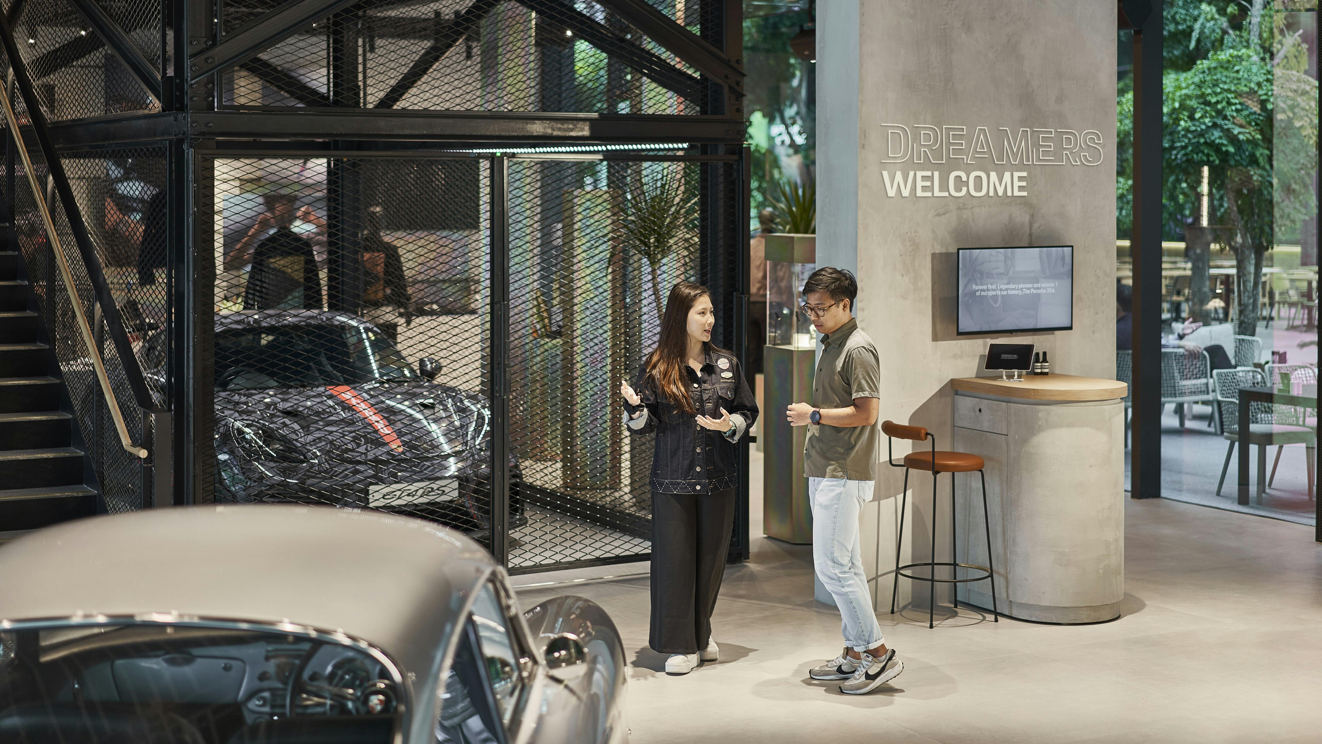 Entrance of Porsche Studio Singapore with a customer greeted by our Guest Experience Lead, with a 718 Cayman GT4 RS on display.