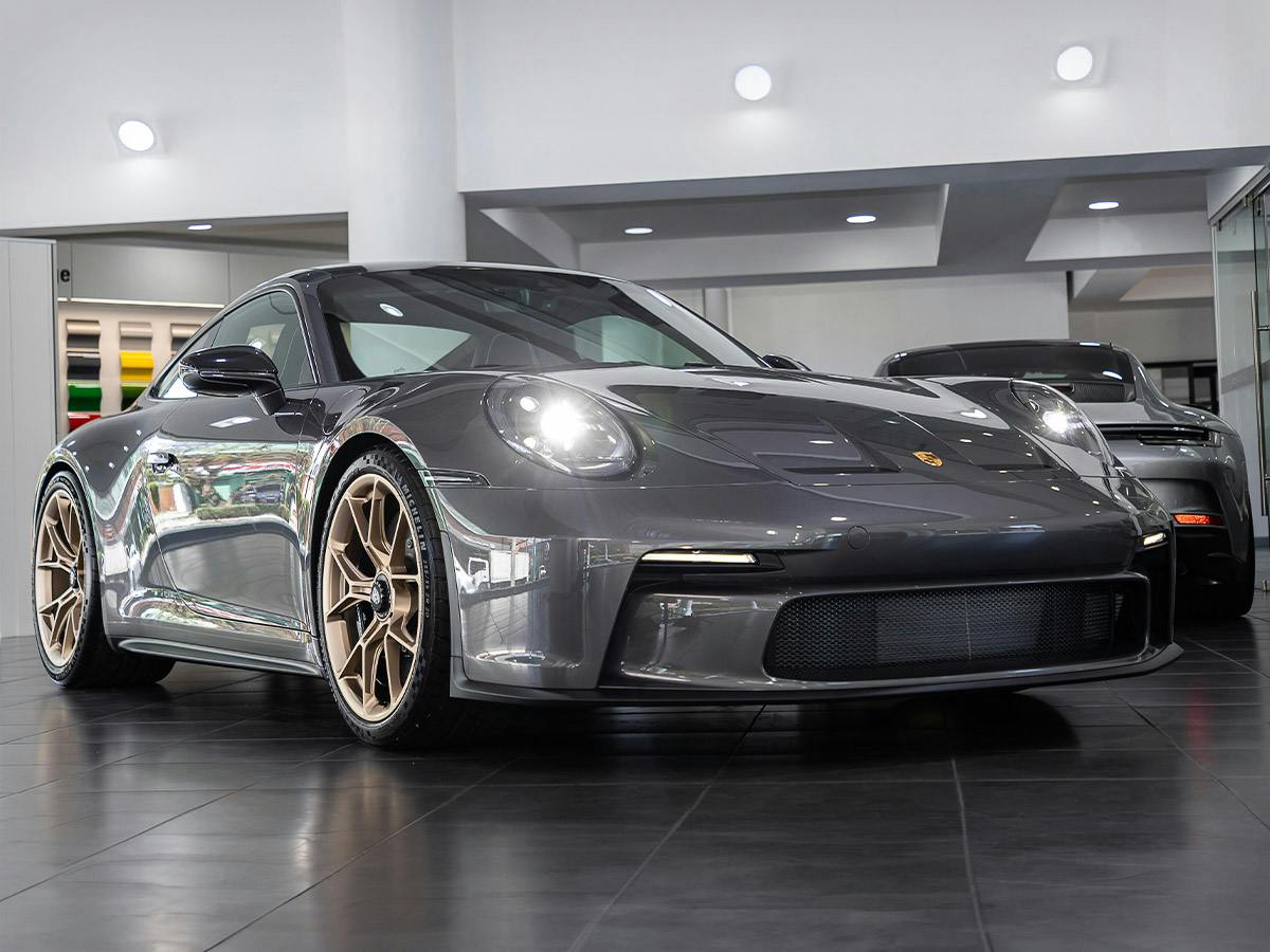Porsche 911 GT3 Touring in Paint to Sample colour Achatgreymetallic with bronze-colored rims, shown from the front in a showroom.