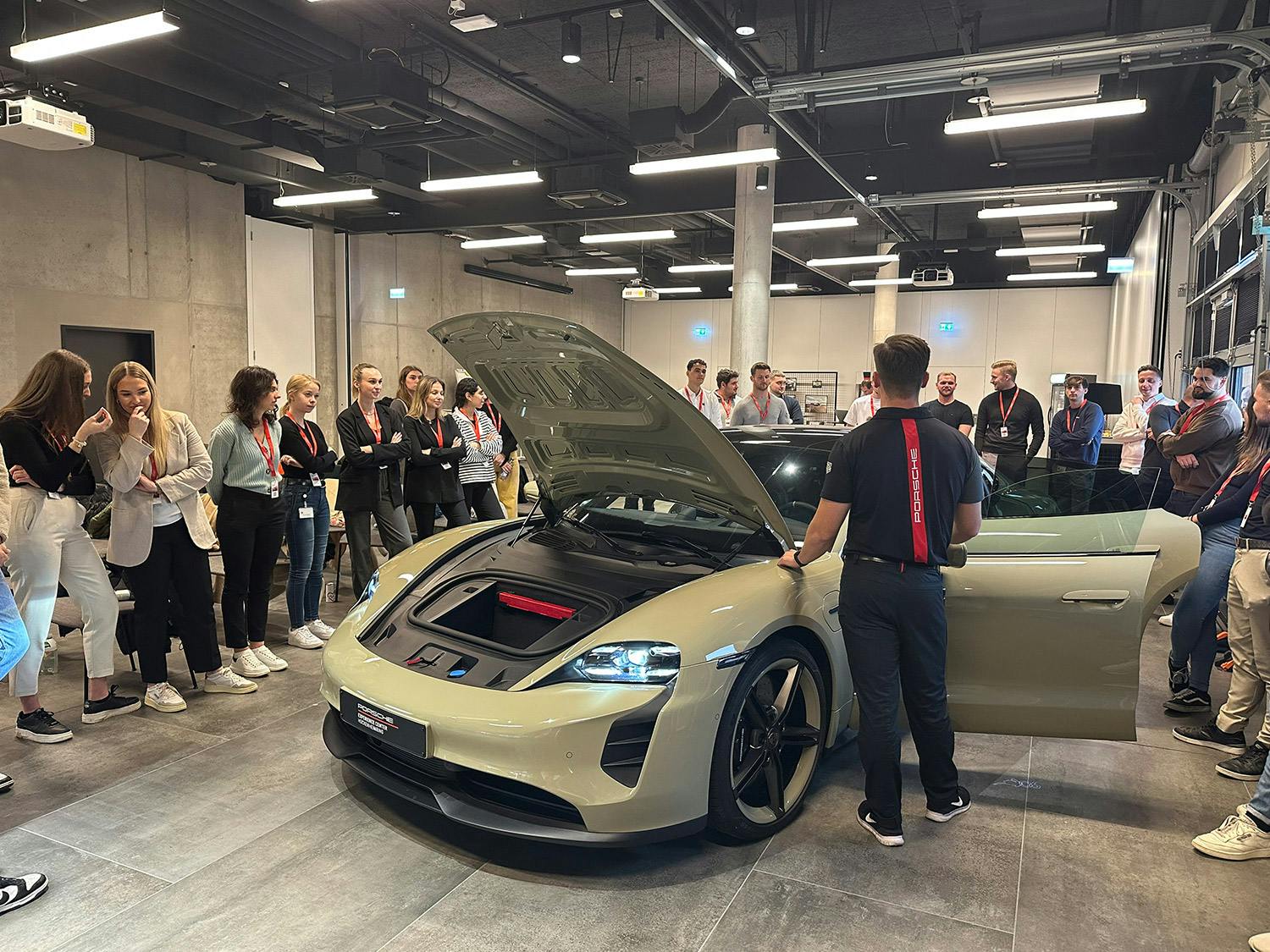Eine Gruppe von Menschen versammelt sich um einen Porsche mit geöffneter Motorhaube.