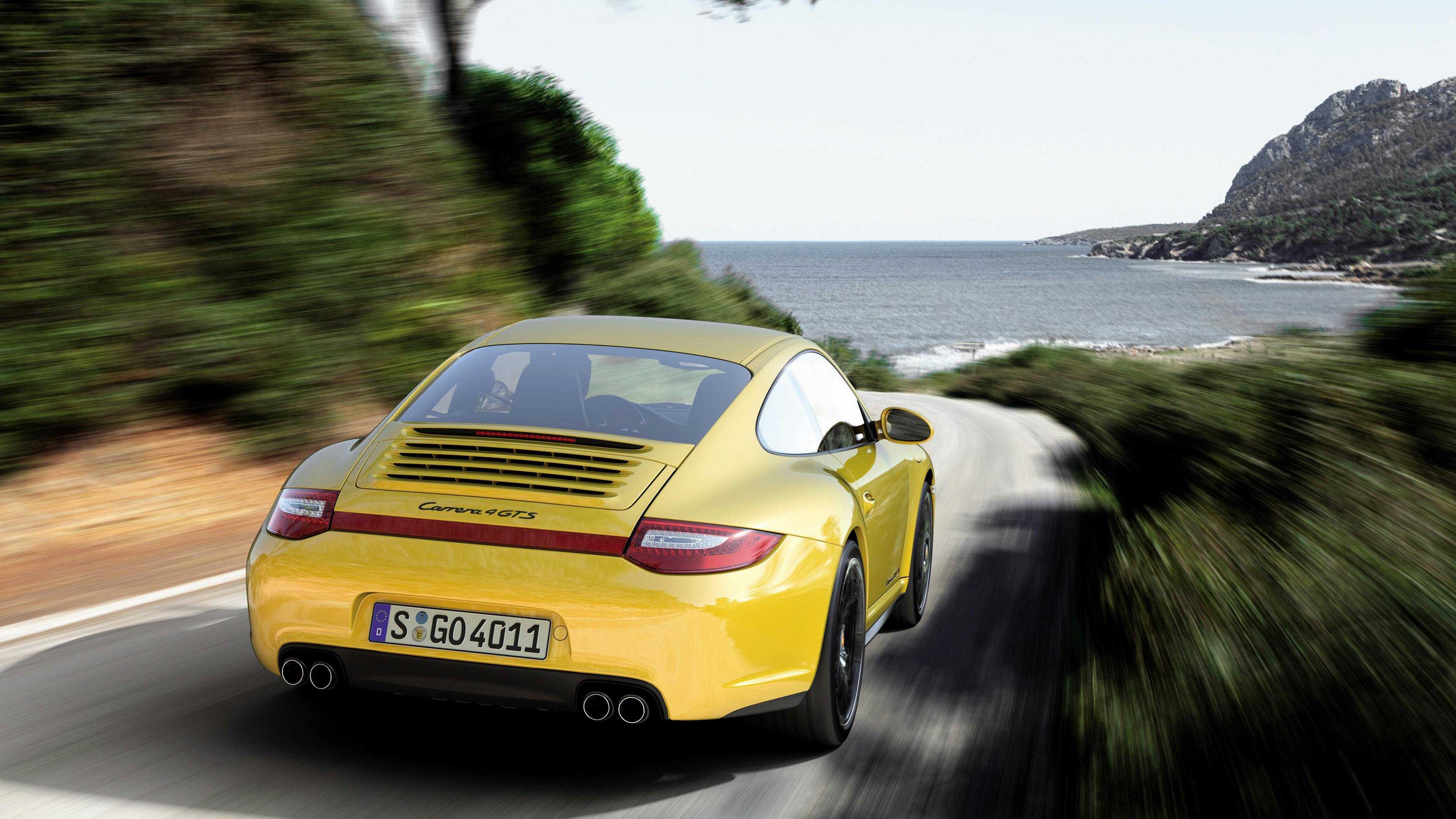 Driving yellow 911 Carrera 4 GTS Coupé type 997 on a coastal road.