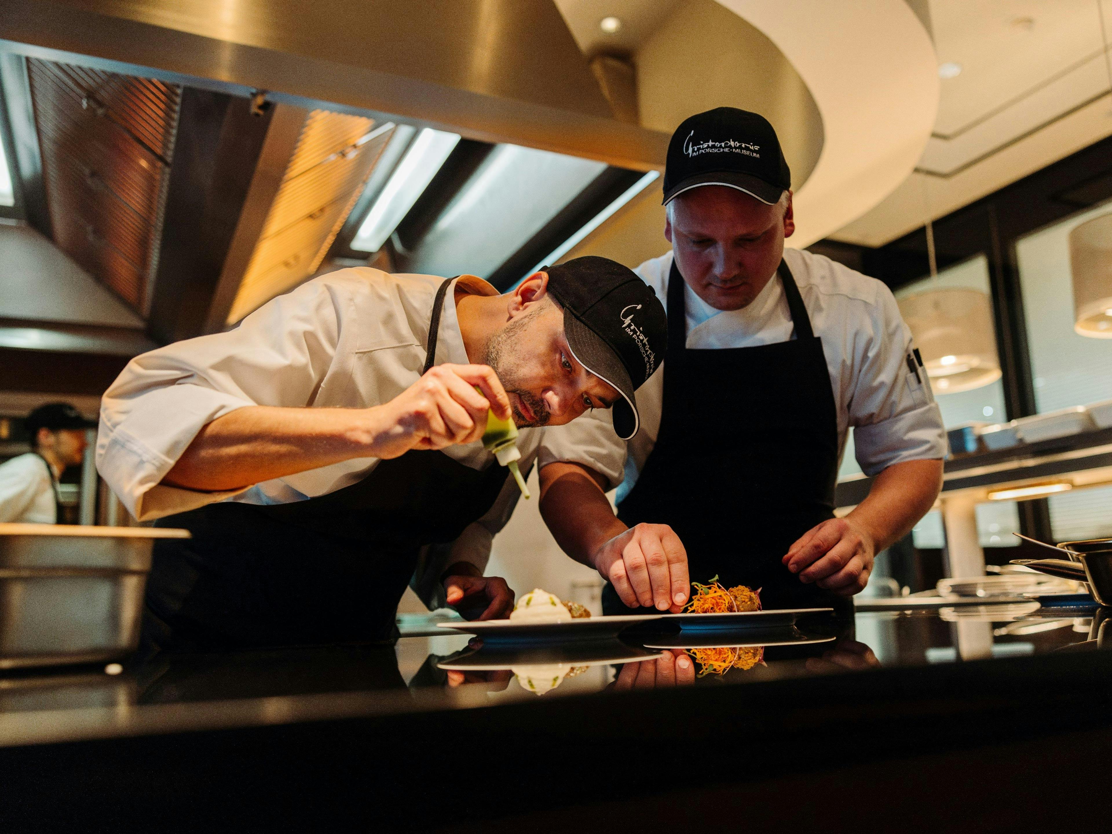 Zwei Köche bereiten liebevoll ein Gourmetmenü in der Porsche Gastronomie zu