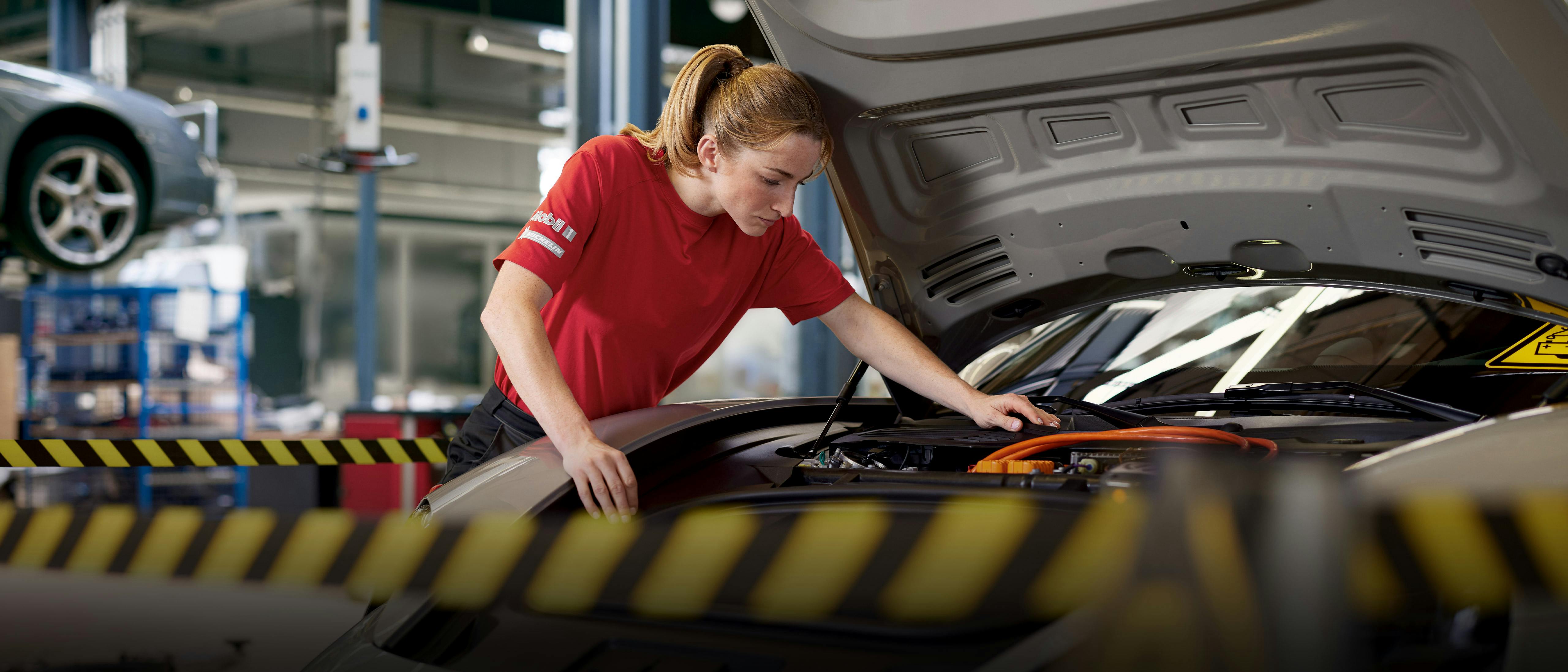 A workshop employee looks under the open bonnet of a Porsche Taycan.