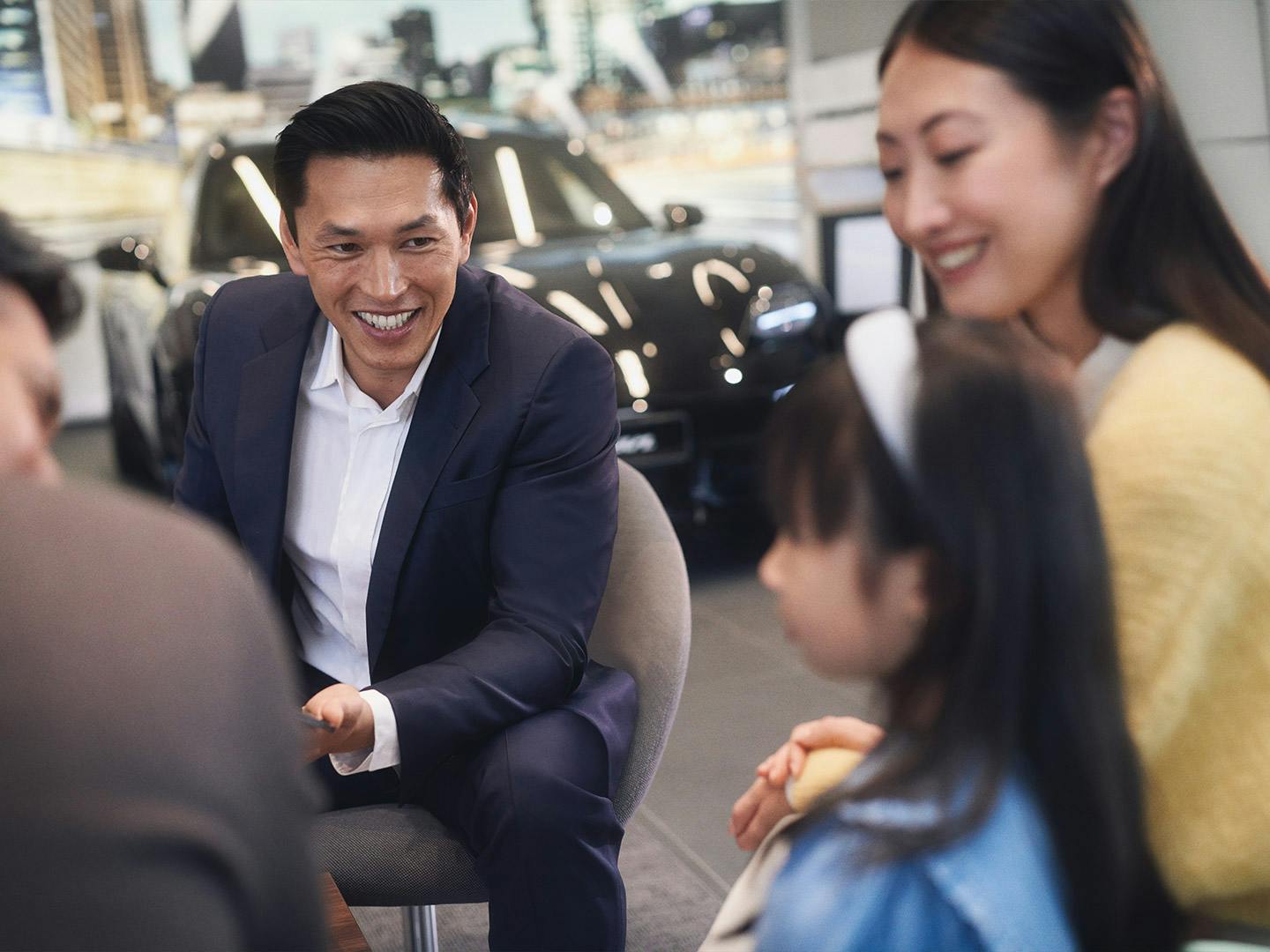 A Porsche employee and a couple in a consultation. A Porsche is in the background.