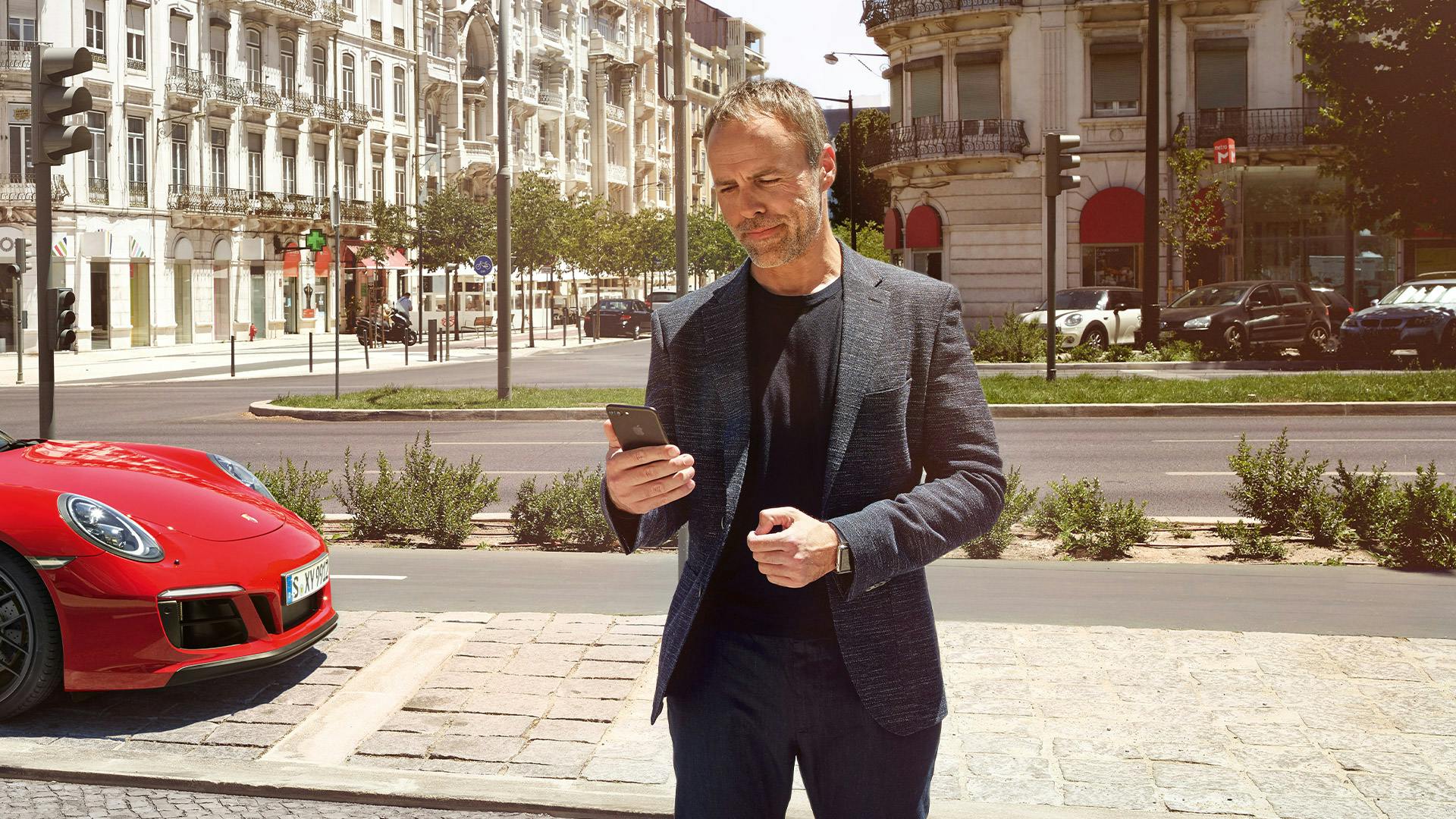 A man looks at his cell phone while standing on a city street.