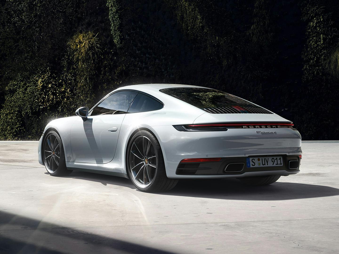 Rear view of a white Porsche 911 in front of a planted wall.