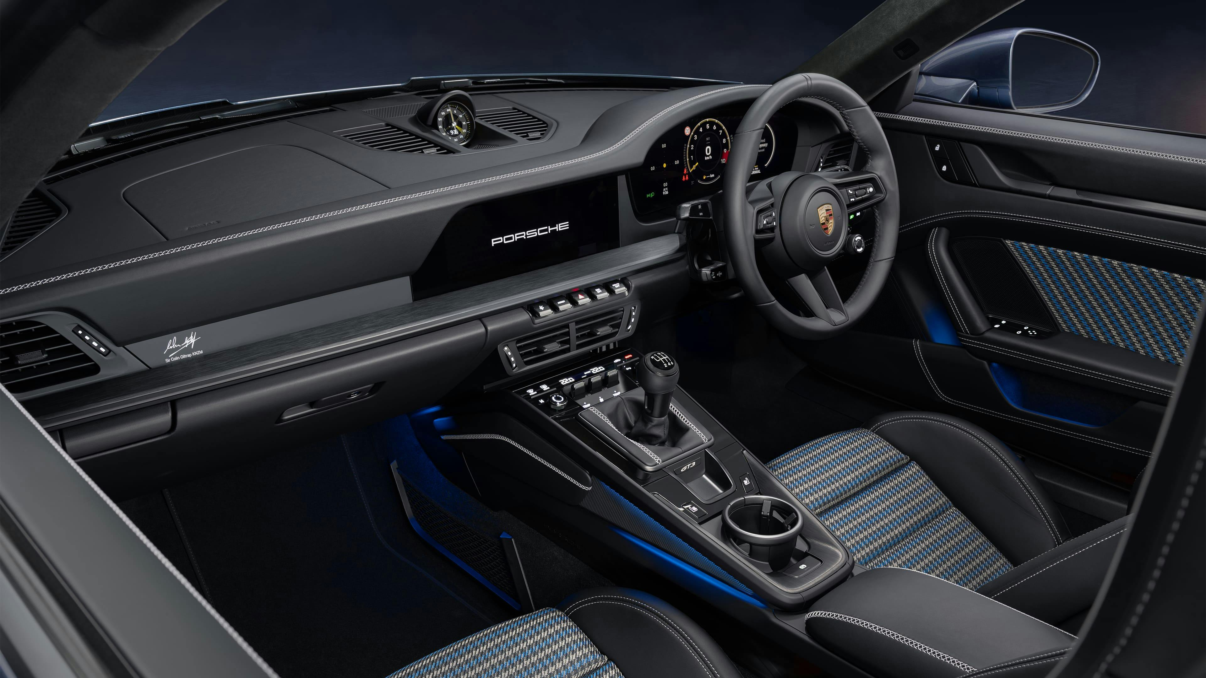 Sports car interior featuring a manual gear lever, black leather trim, and patterned seats with blue accents.