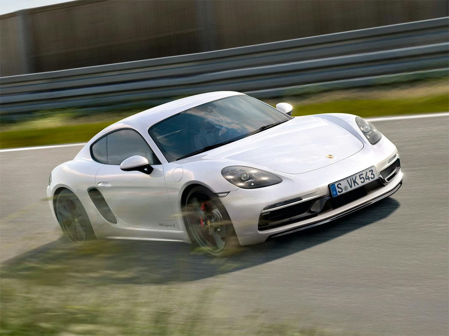 A white Porsche 718 Cayman driving along a track.