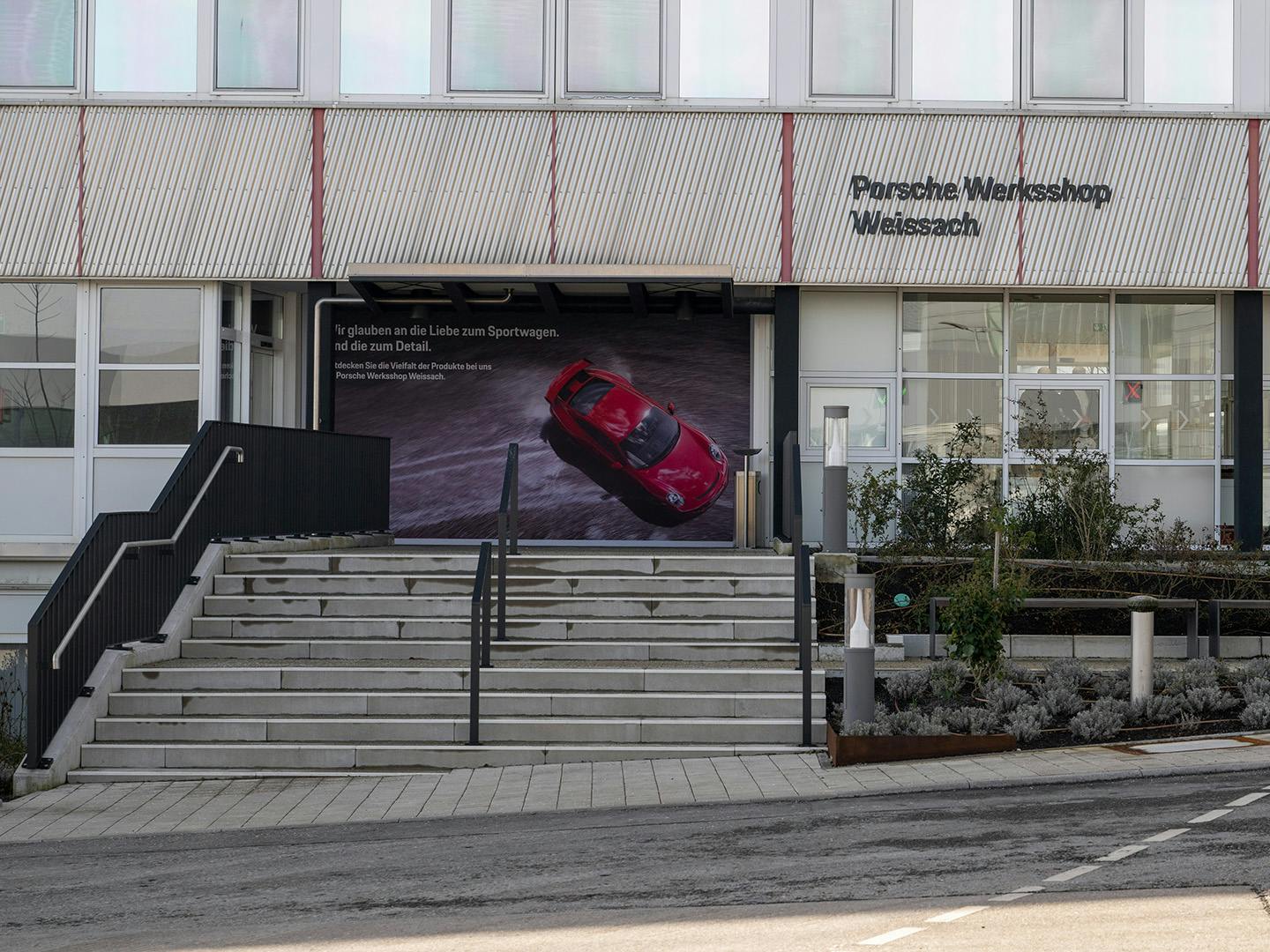 Main entrance with wide staircase. Above the entrance, the logo for Porsche Werksshop Weissach is attached to the facade.