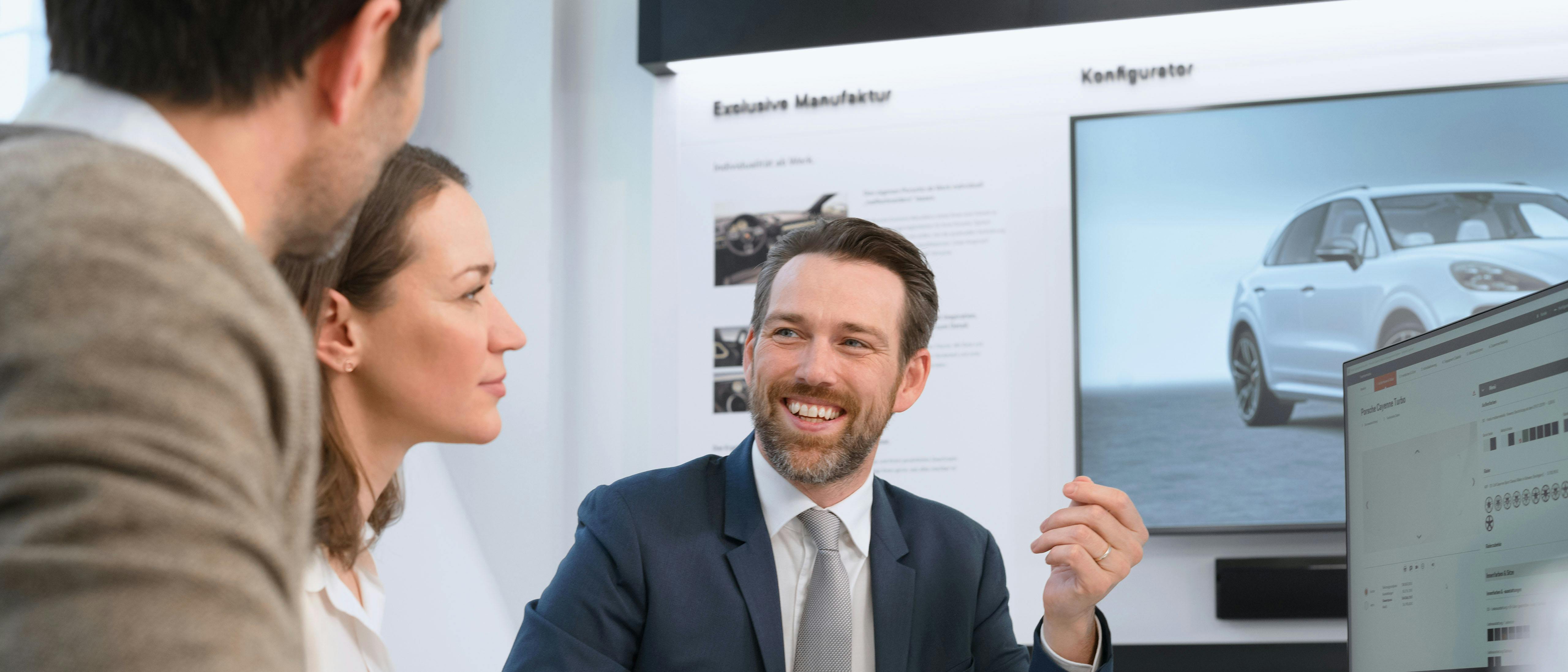 Ein Porsche Verkäufer berät an einem Bildschirm zwei Kunden.