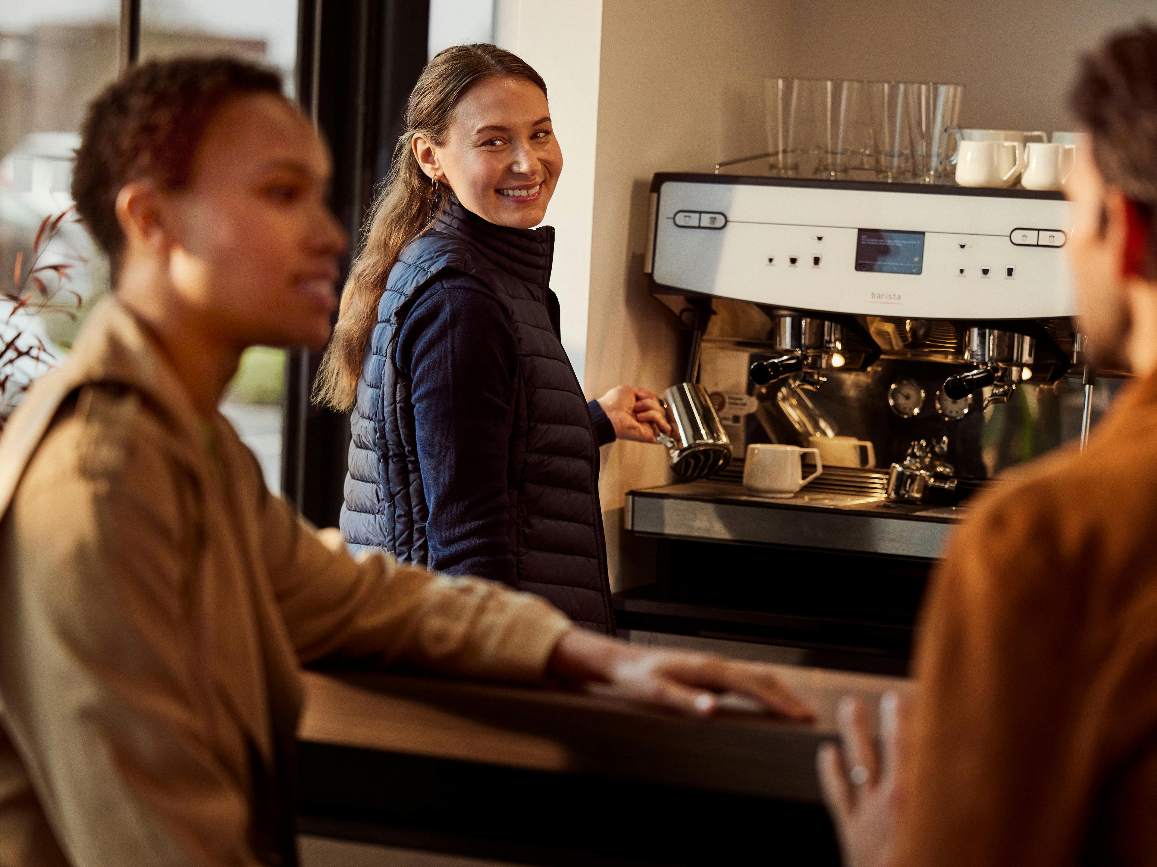 A member of staff at a Porsche Centre stood by the coffee machine while a customer waits for their drink.
