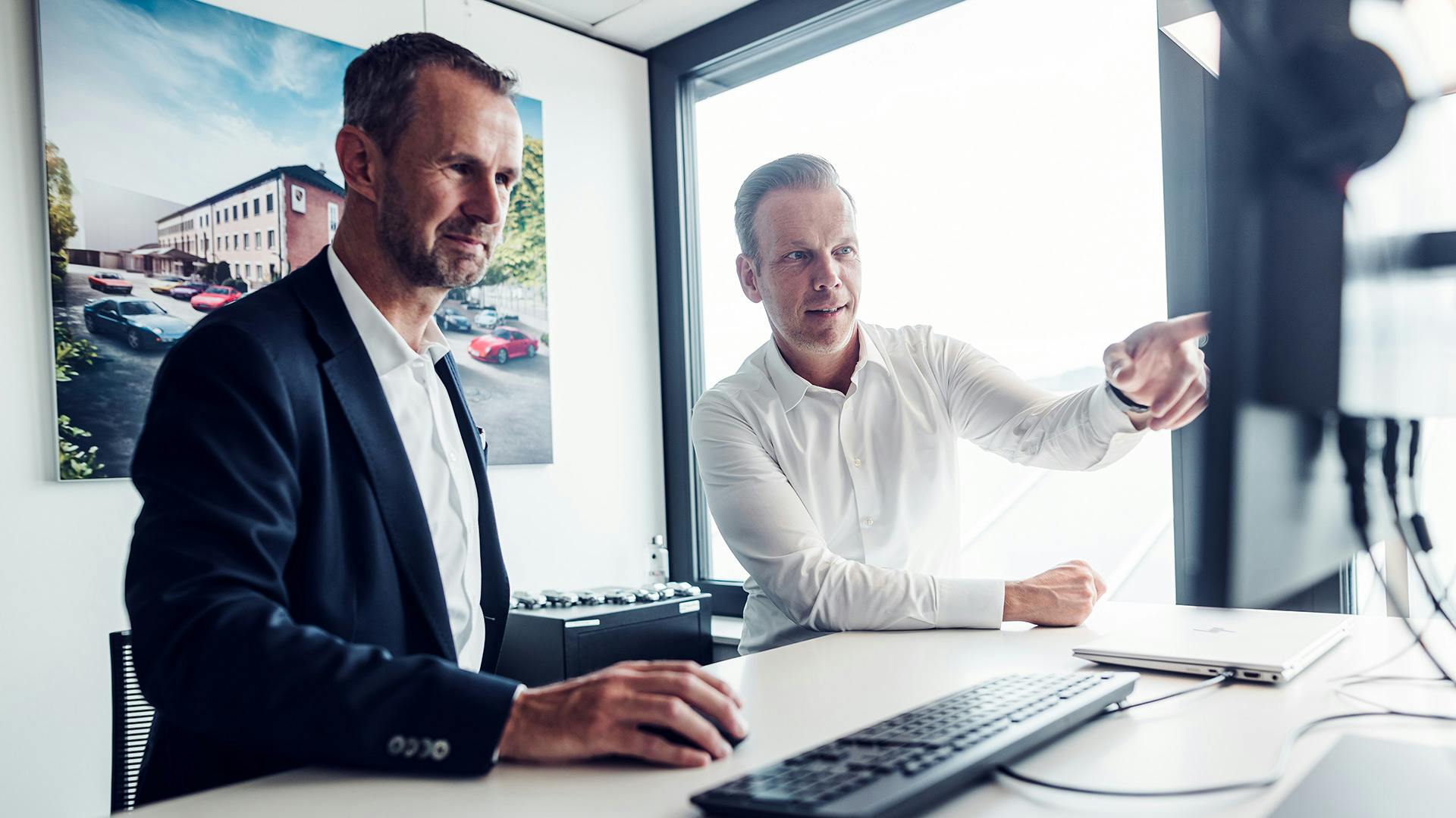 Zwei Männer sitzen an einem Computer, einer von ihnen zeigt auf einen Bildschirm.