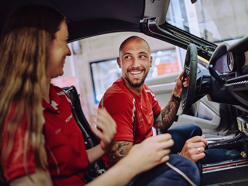 Dos empleados de Porsche están sentados en un vehículo y hablan.