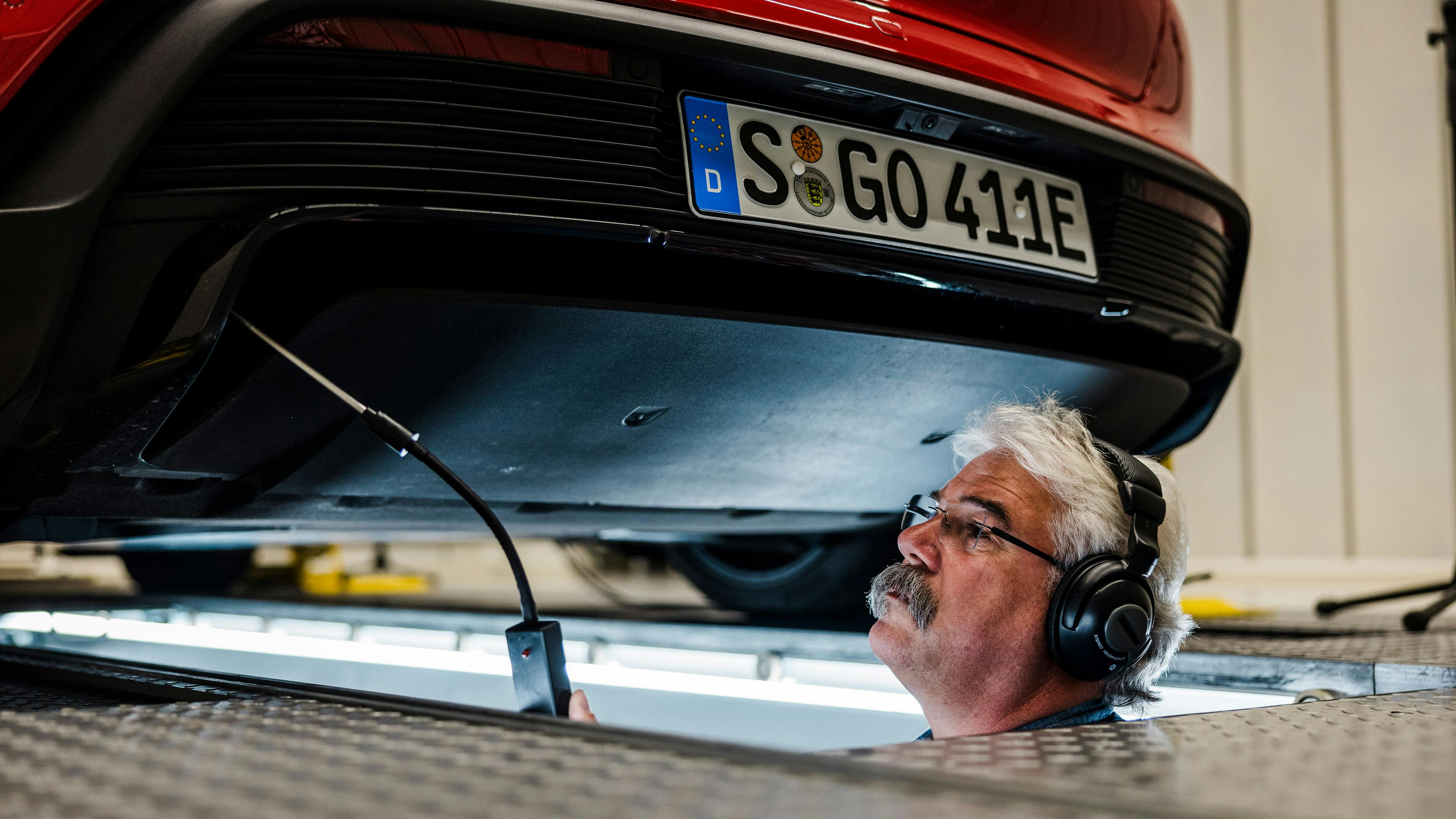 Ein Porsche Mitarbeiter steht unter einem Fahrzeug auf einer Hebebühne und vollzieht eine technische Prüfung.