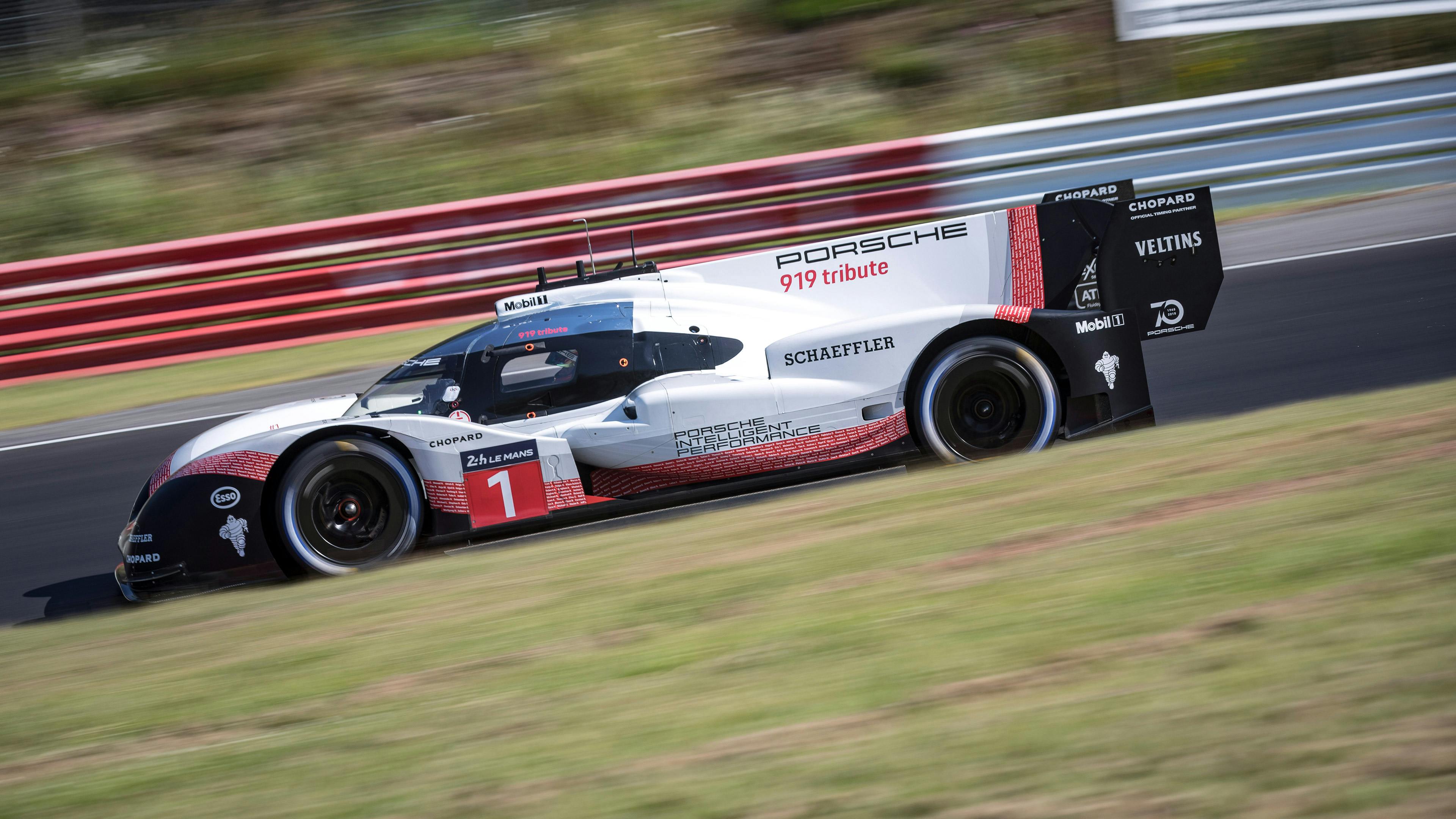 A white Porsche race car competing at speed on a circuit, captured with motion blur conveying high velocity.