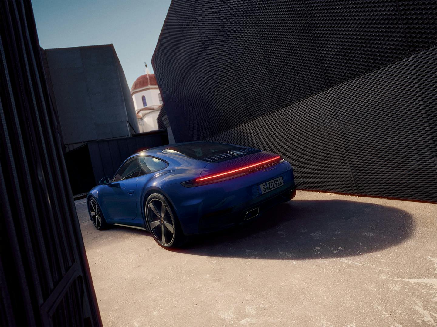 Porsche 911 Carrera staat geparkeerd tussen twee gebouwen.