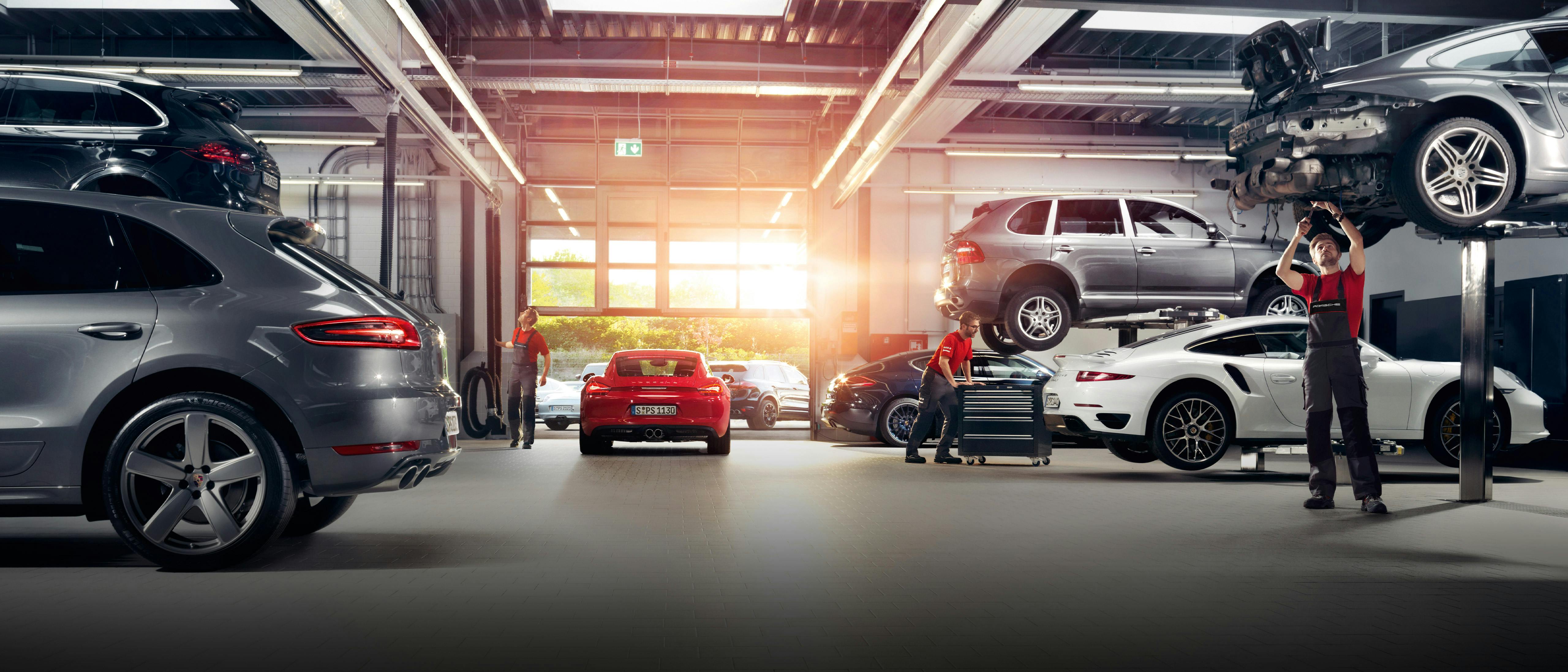 Mecánicos trabajando en un taller Porsche con diferentes vehículos.