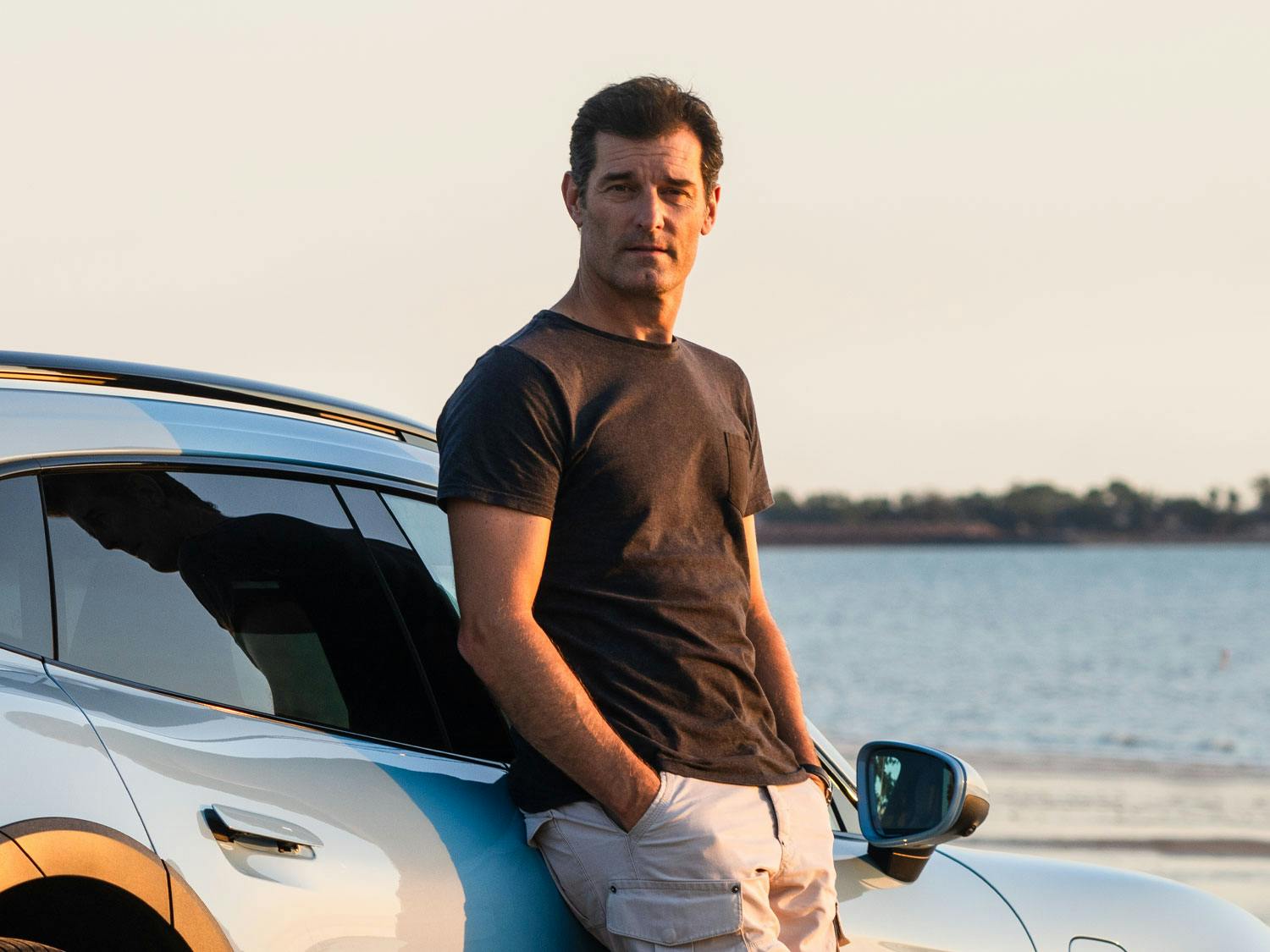 Mark Webber leaning on a car looking at the camera with his hands in his pockets